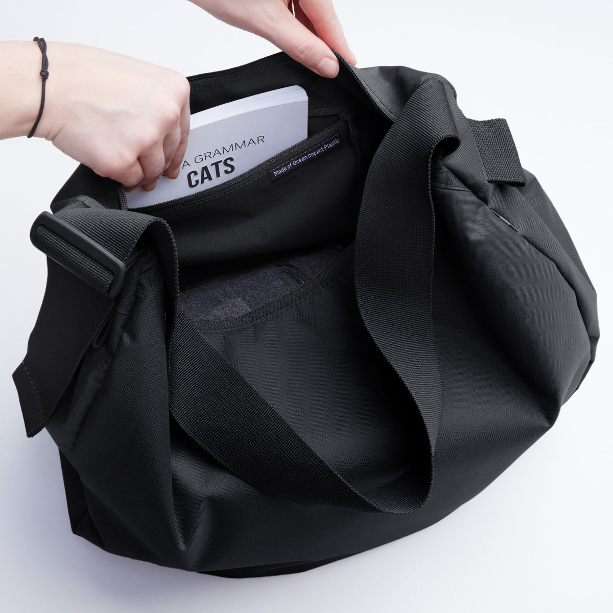 CURVED BAG Tasche in black (Schwarz) von einer Frau, die ein Buch in die Innentasche legt.
