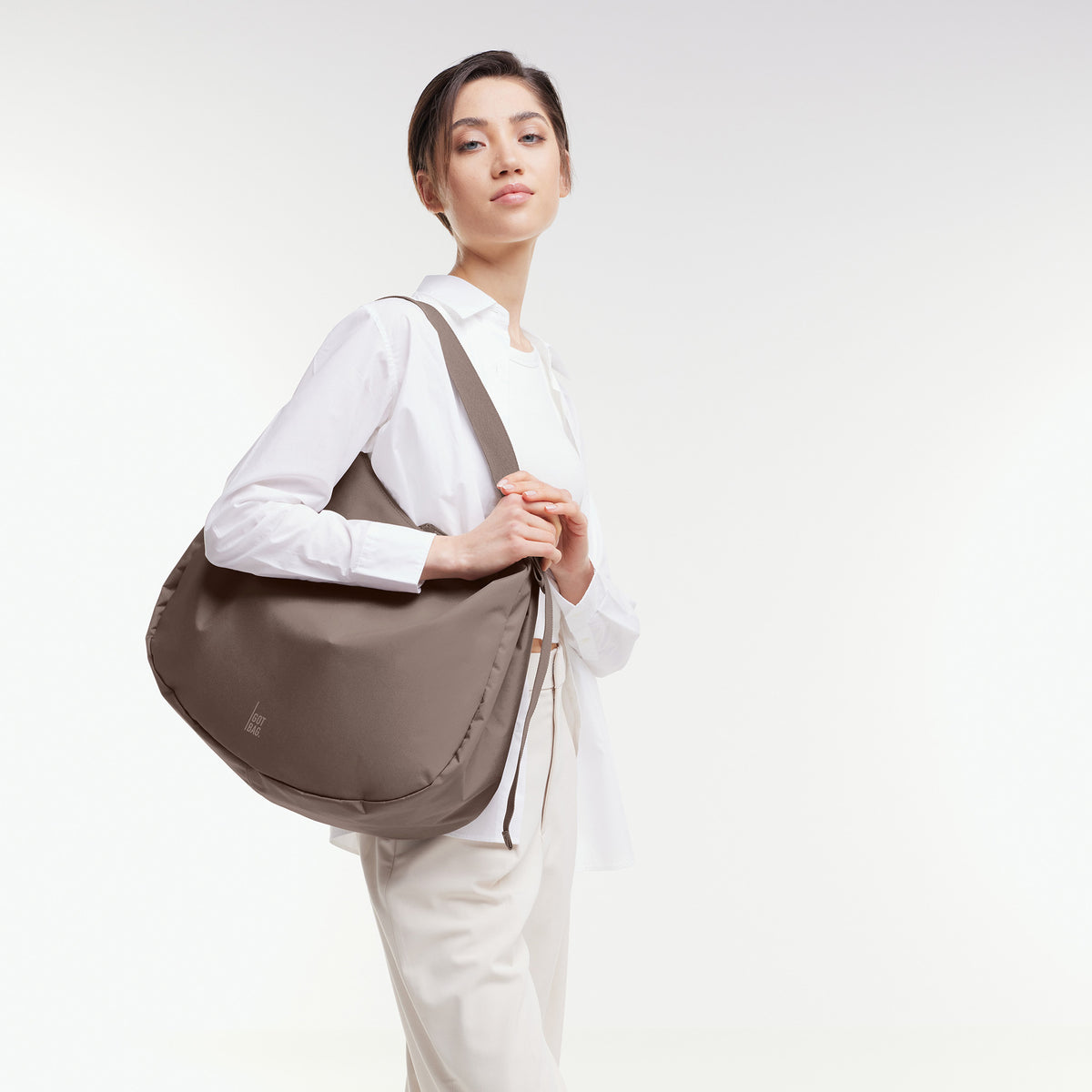 CURVED BAG Tasche in oyster (klassisches Taupe-Braun) von einer Frau über der Schulter getragen.