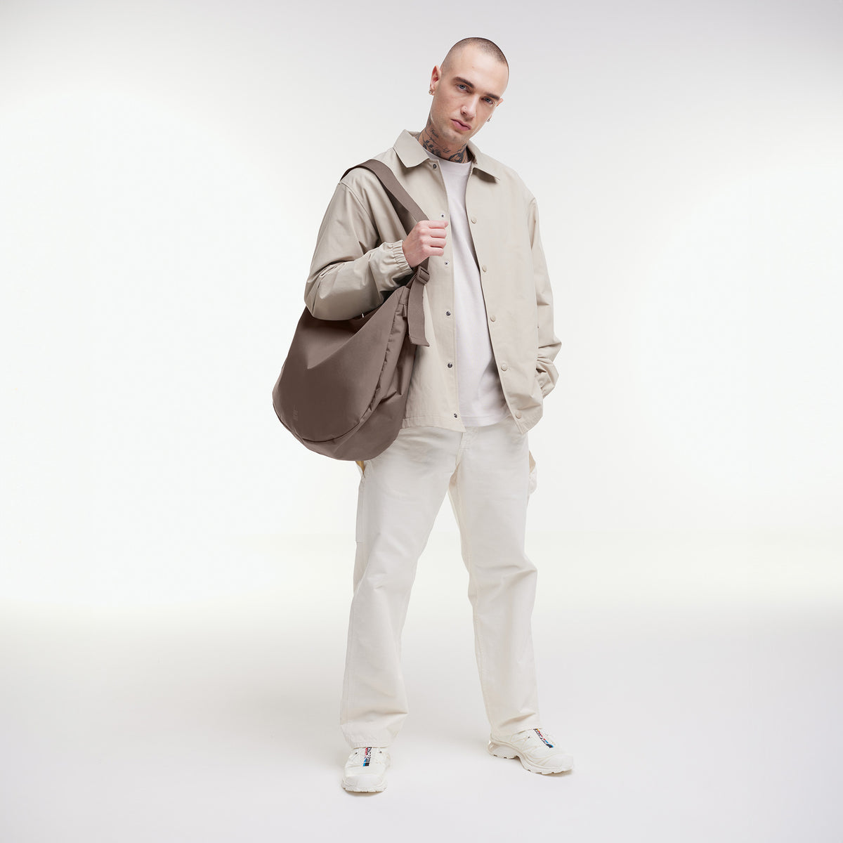 CURVED BAG Tasche in oyster (klassisches Taupe-Braun) von einem Mann über der Schulter getragen.