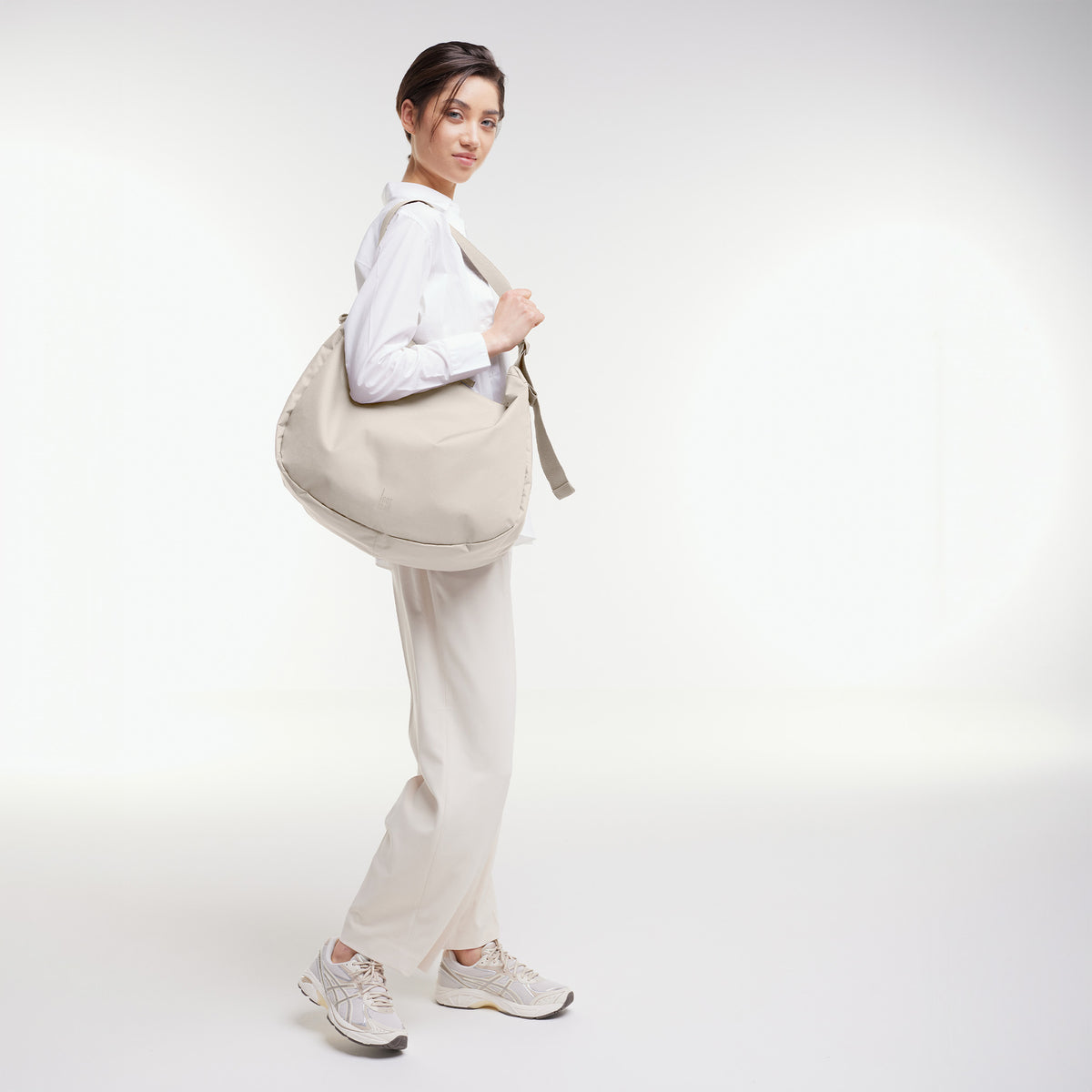 CURVED BAG Tasche in soft shell (warmes Cremeweiß) von einer Frau über der Schulter getragen.