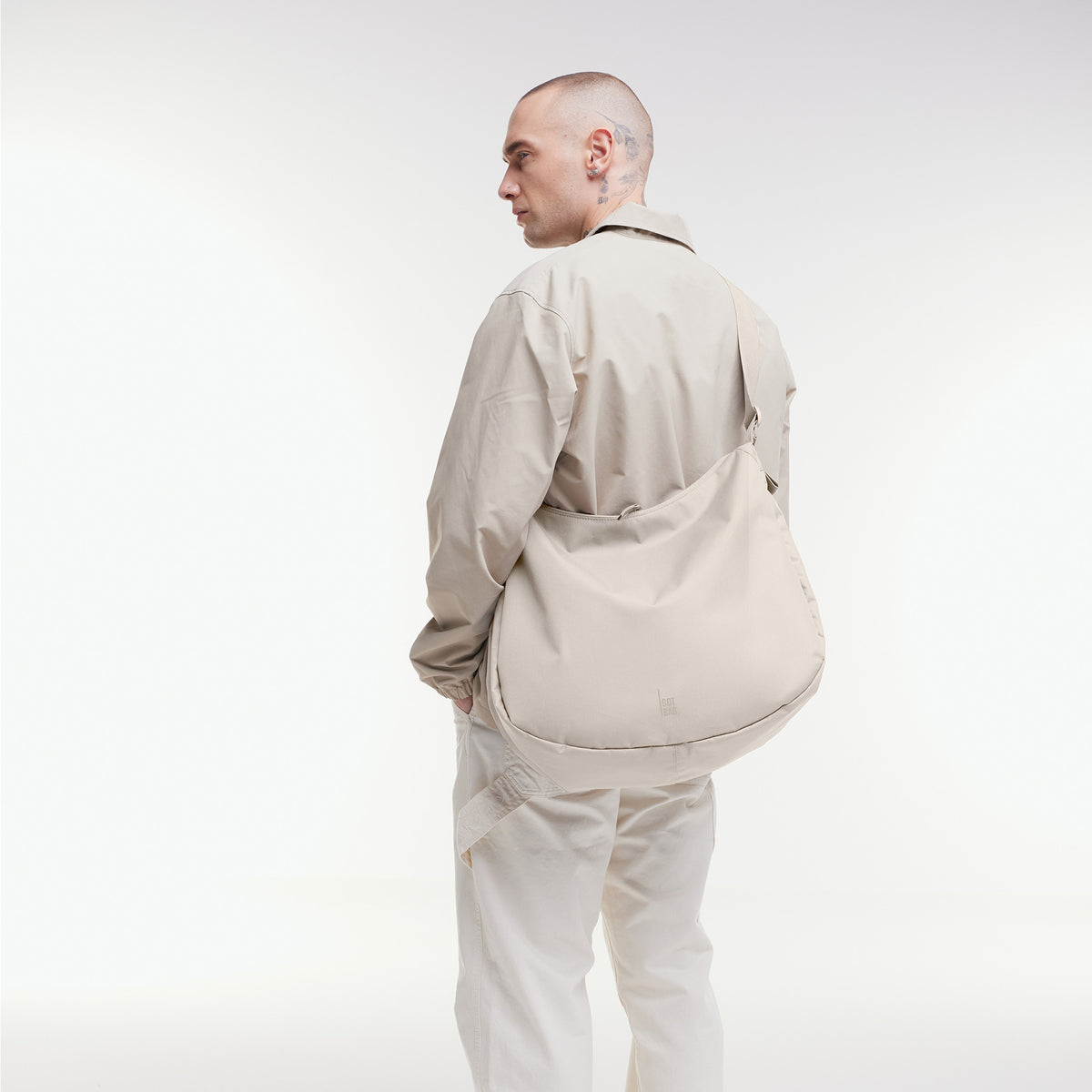CURVED BAG Tasche in soft shell (warmes Cremeweiß) von einem Mann crossbody getragen.