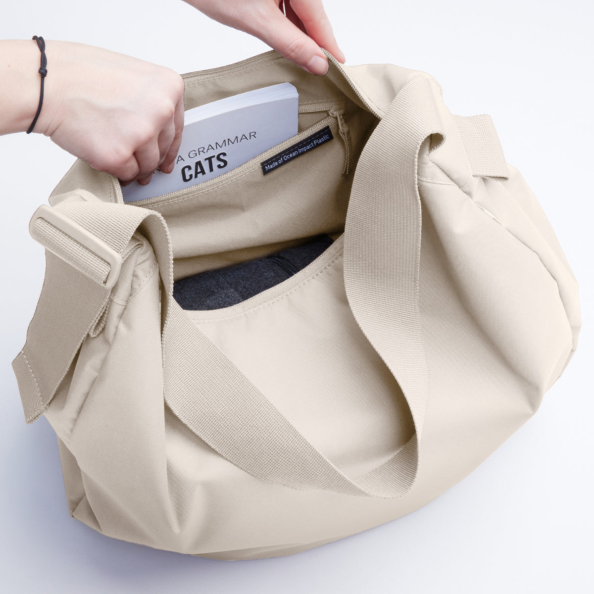 CURVED BAG Tasche in soft shell (warmes Cremeweiß), von einer Frau, die ein Buch hineinlegt.
