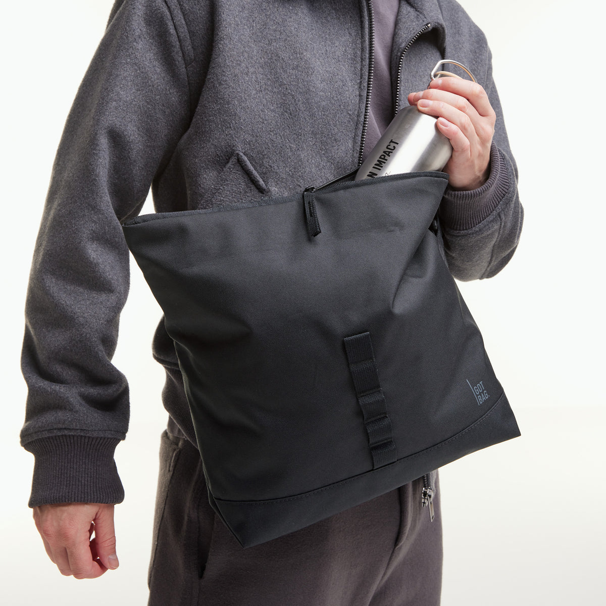 MESSENGER BAG Tasche in black (Schwarz) von einem Mann getragen, der eine Flasche hält.