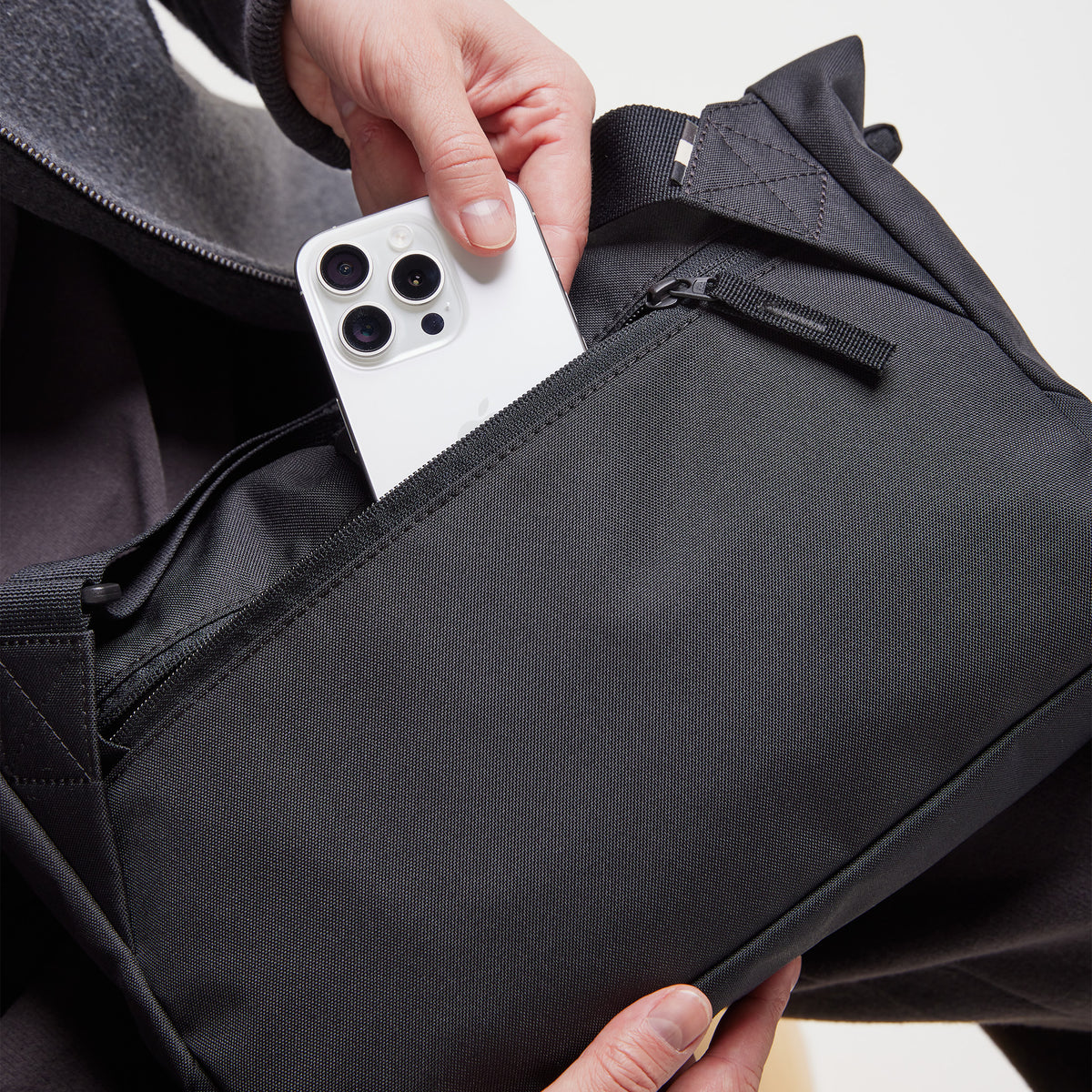 MESSENGER BAG Tasche in black (Schwarz), von einer Frau benutzt, die ein Handy hineinsteckt.
