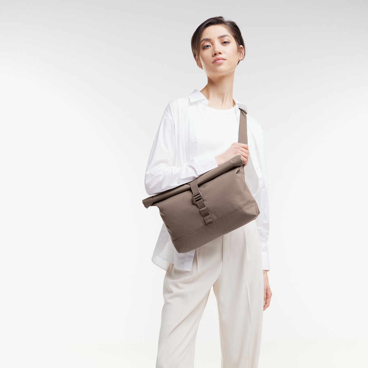 MESSENGER BAG Tasche in oyster (klassisches Taupe-Braun) von einer Frau über der Schulter getragen.