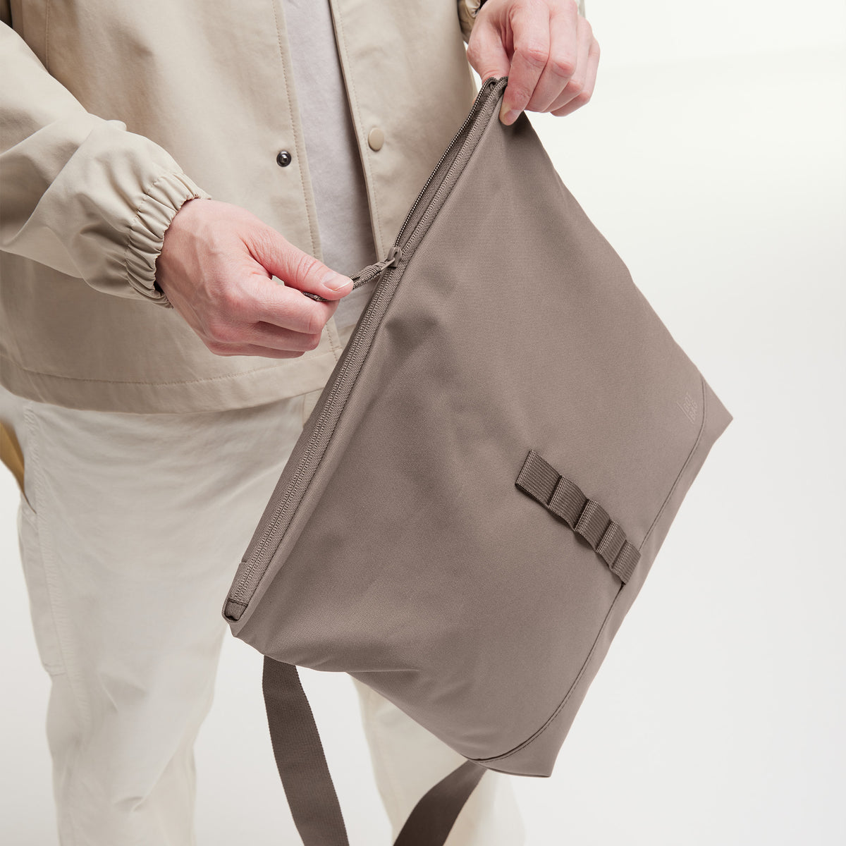 MESSENGER BAG Tasche in oyster (klassisches Taupe-Braun) von einem Mann in der Hand gehalten.