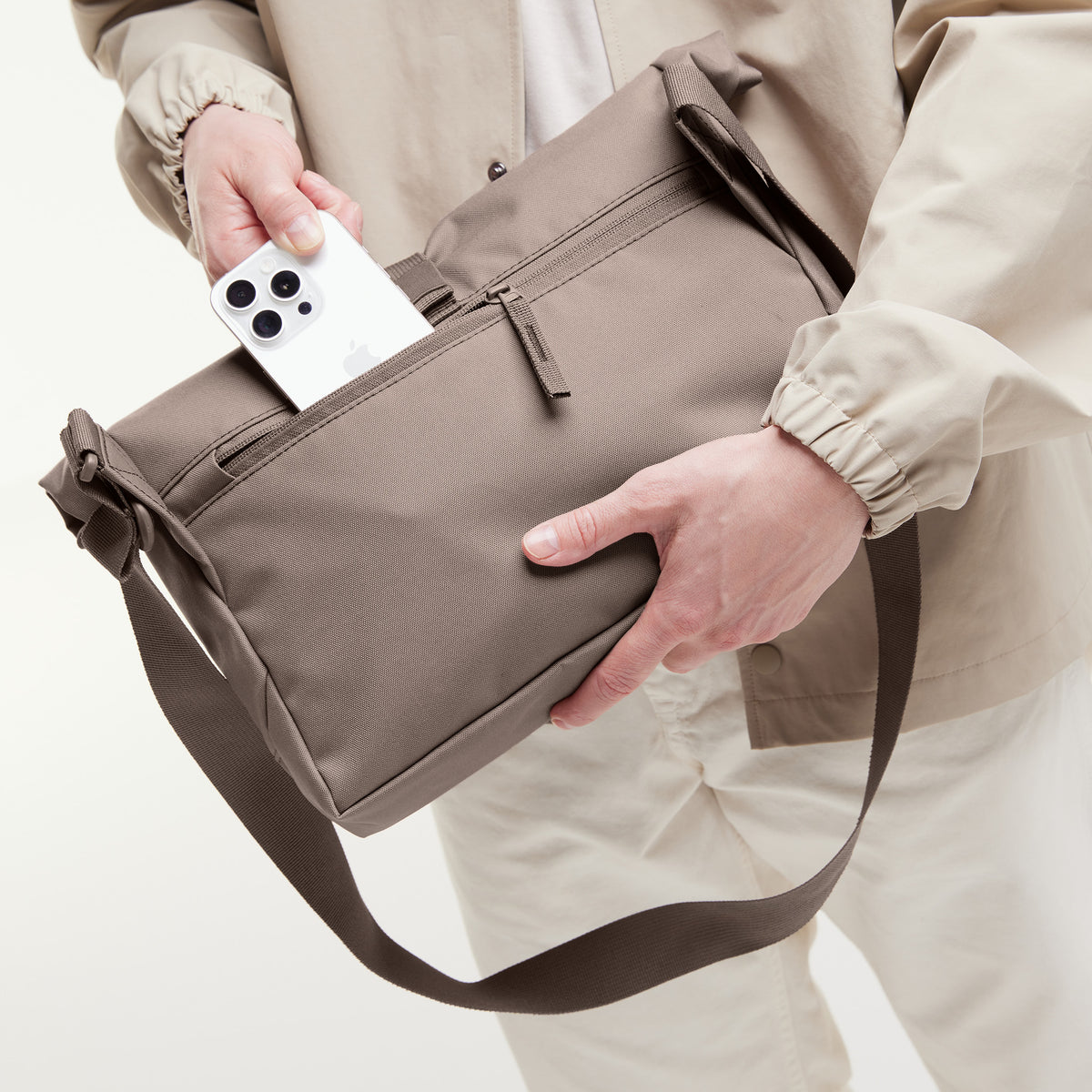 MESSENGER BAG Tasche in oyster (klassisches Taupe-Braun) von einem Mann in den Händen gehalten.