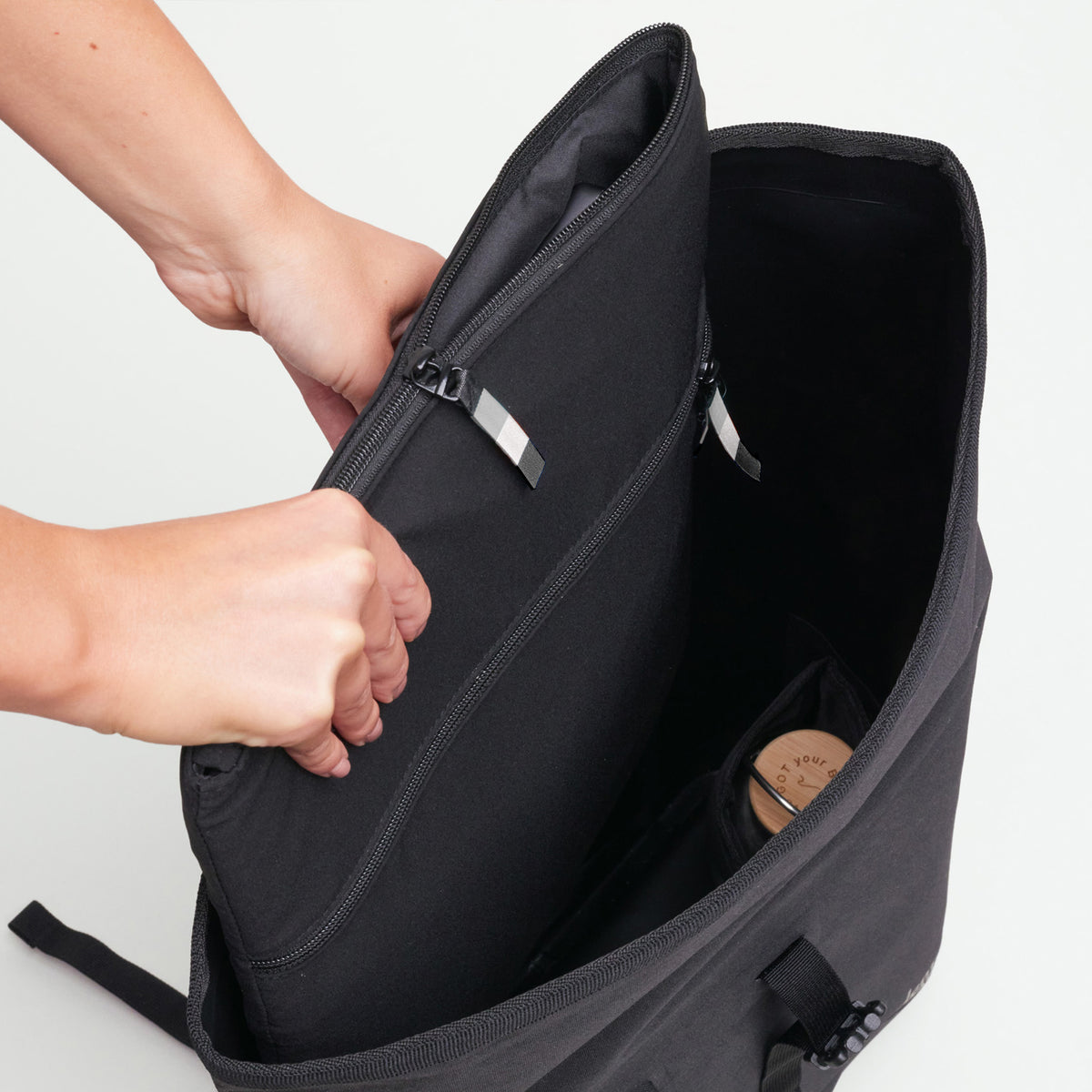 ROLLTOP 2.0 MONOCHROME EDITION Rucksack in black (Schwarz), dessen oberes Fach von Händen geöffnet wird.