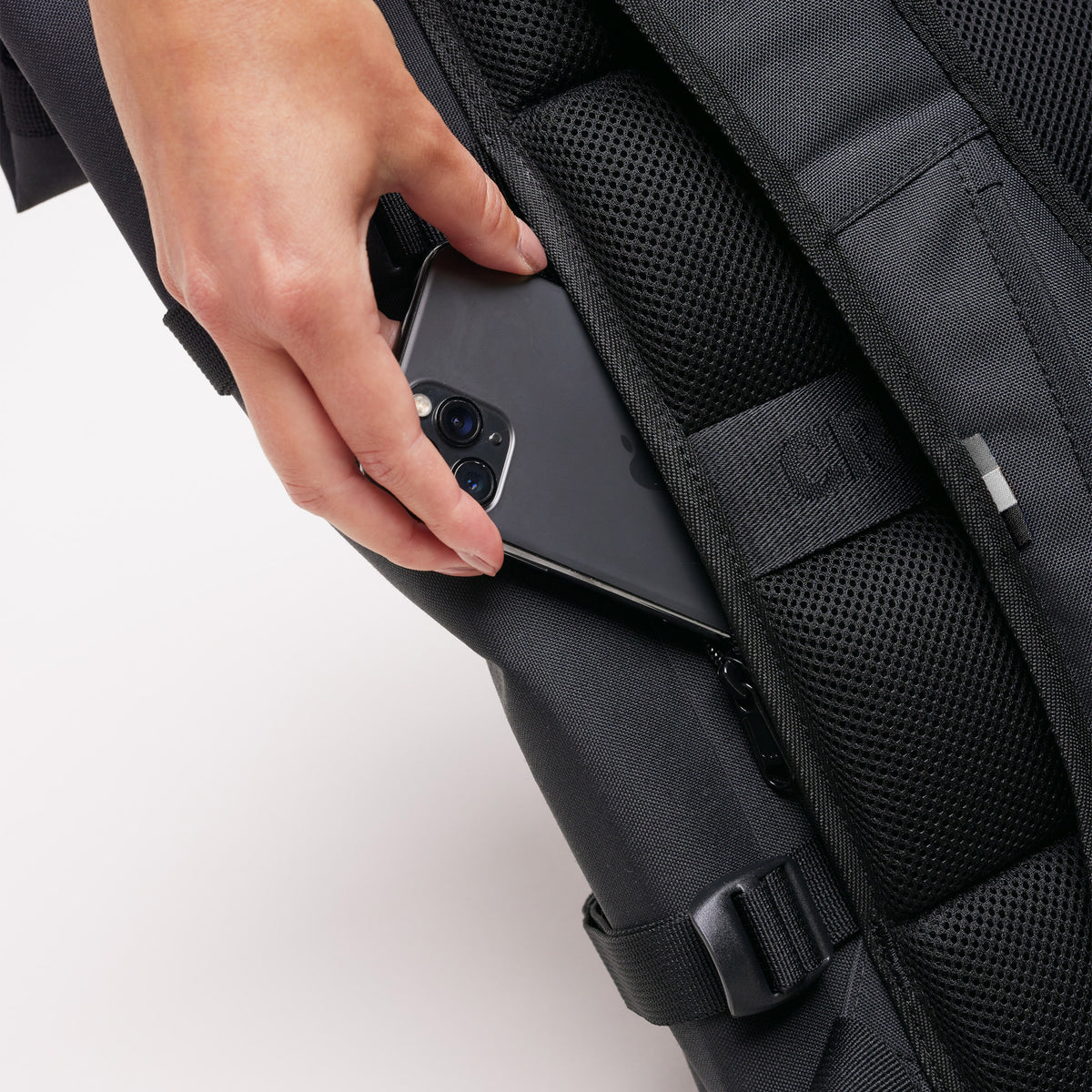 ROLLTOP 2.0 Monochrome Edition Rucksack in black (Schwarz), eine Frau steckt ein Telefon in die Seitentasche.
