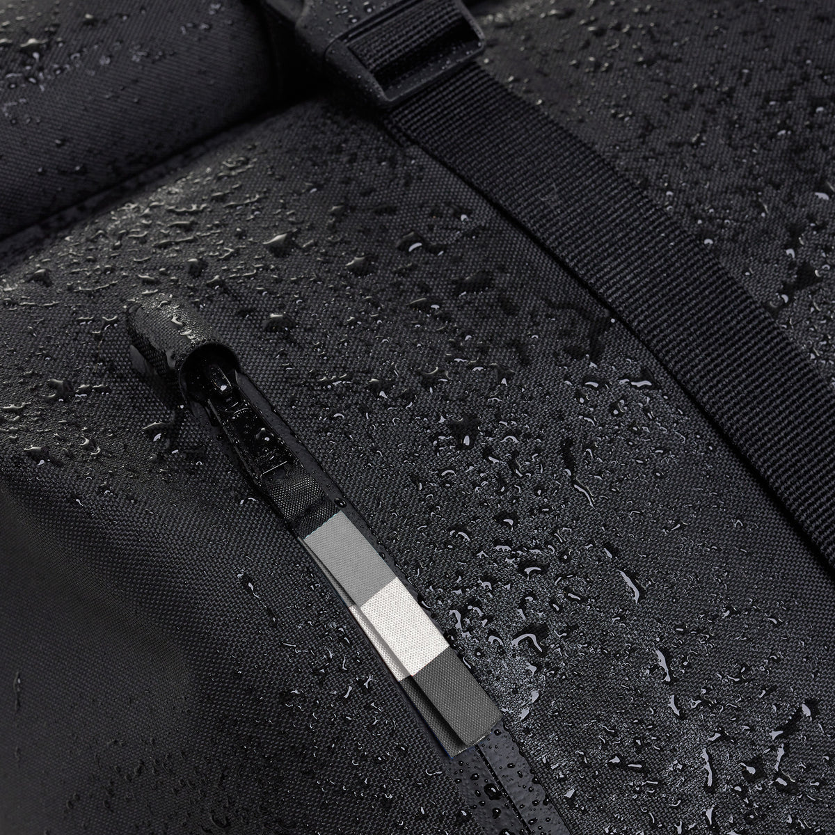 ROLLTOP Rucksack in black (Schwarz) mit Wassertropfen auf dem Gewebe und Reißverschluss, Detailaufnahme.