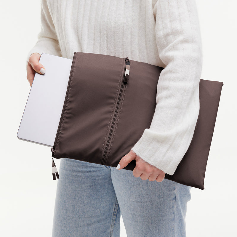 ROLLTOP Tasche in tadpole (Schokobraun) von einer Frau gehalten, die einen Laptop einsteckt.