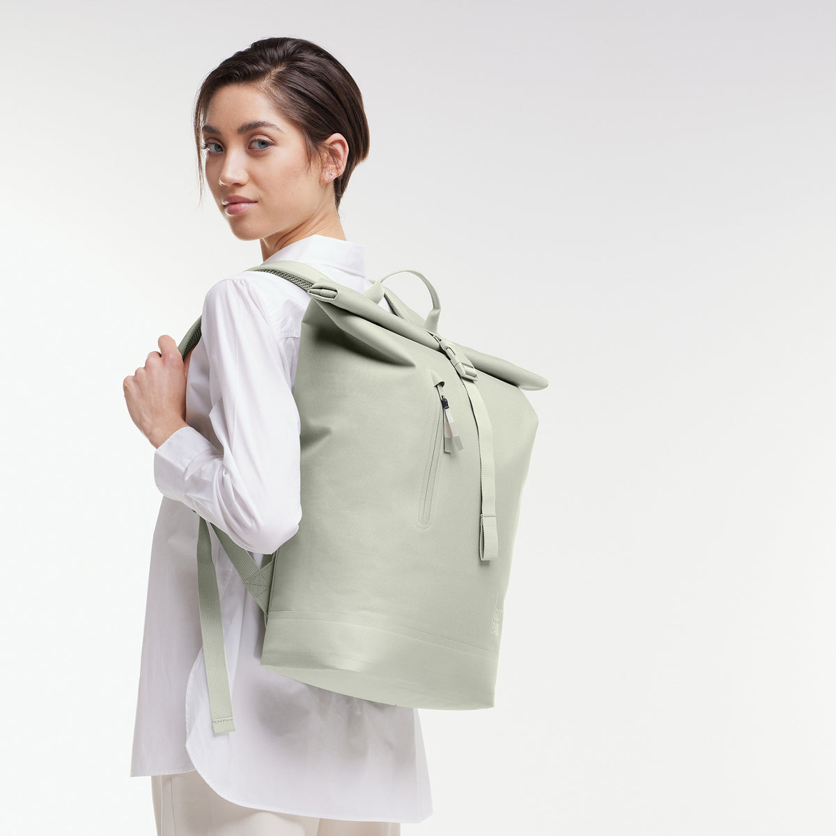ROLLTOP LITE Rucksack in porpoise (helles Grau mit frischem grünen Unterton) von einer Frau als Rucksack auf dem Rücken getragen.