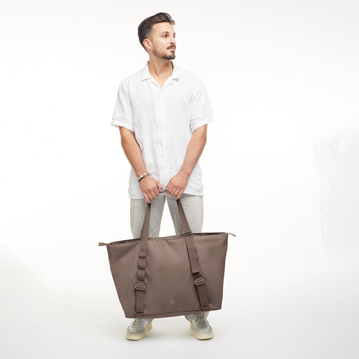 TOTE BAG Tasche in oyster (klassisches Taupe-Braun) von einem Mann in der Hand gehalten.