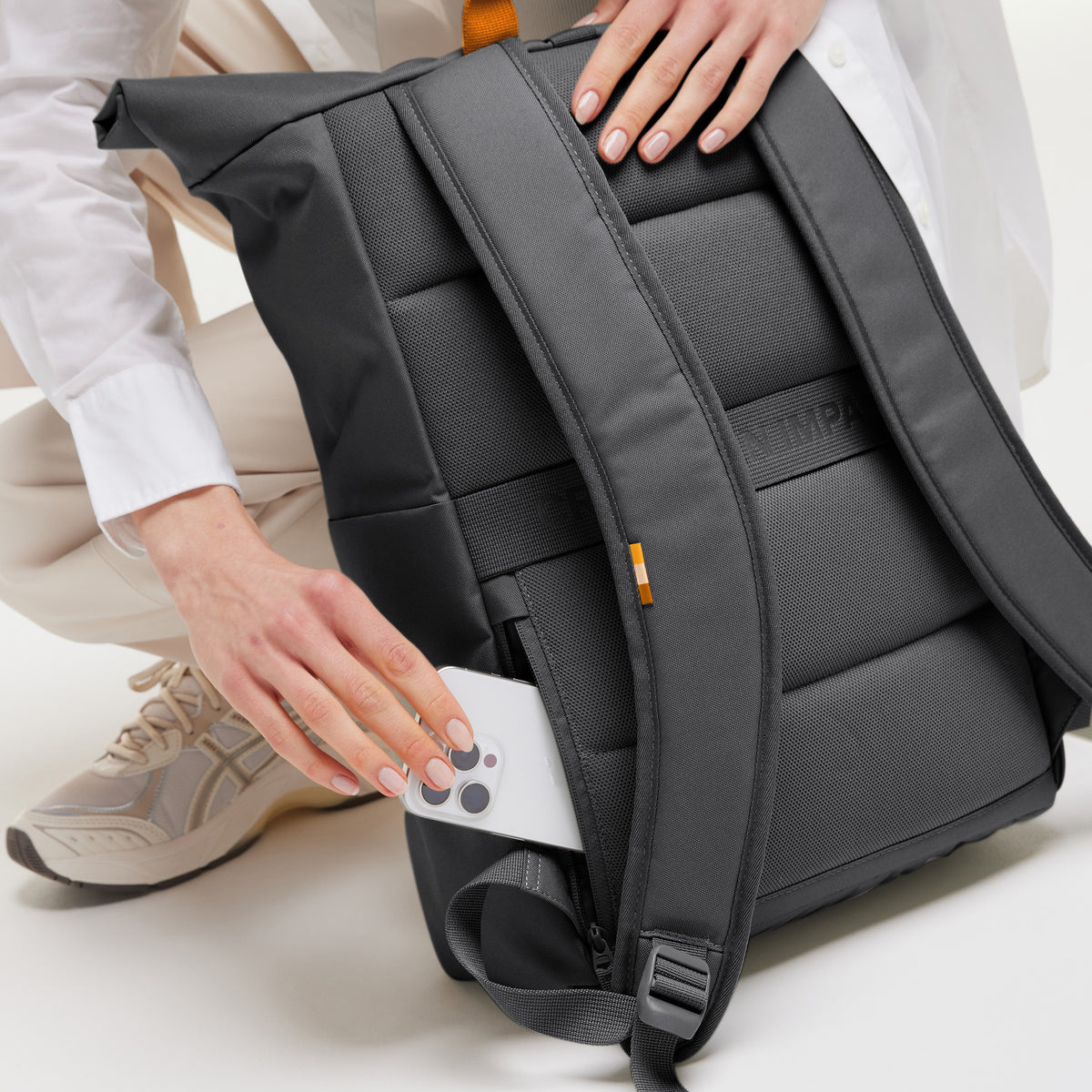 ROLLTOP EASY Rucksack in shark (Dunkelgrau), eine Frau steckt ein Smartphone in die Seitentasche.