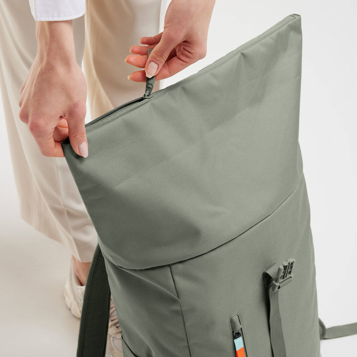 ROLLTOP EASY Rucksack in bass (Salbeigrün) von einer Frau am Reißverschluss geöffnet.