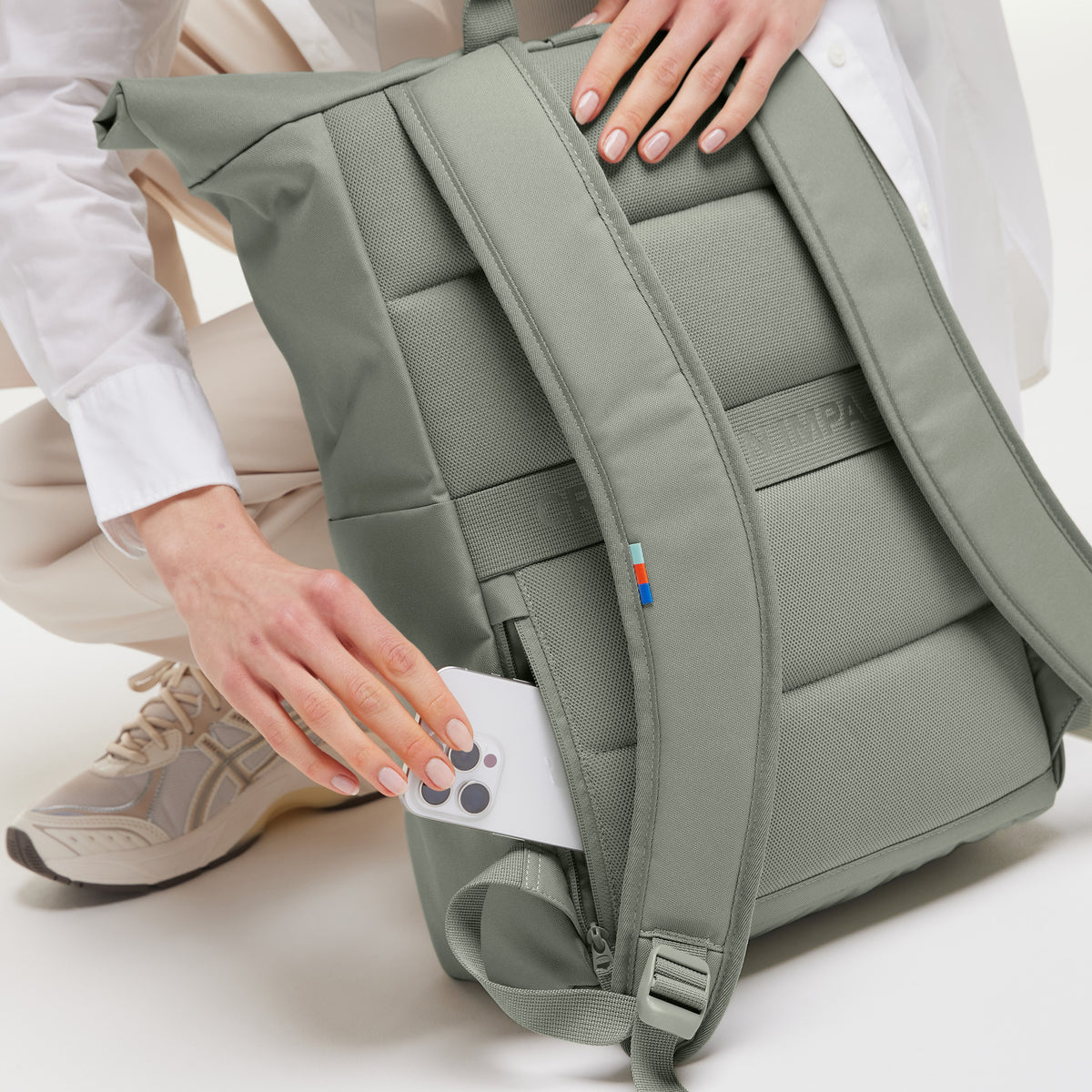ROLLTOP EASY Rucksack in bass (Salbeigrün), eine Frau nimmt ein Handy aus der Seitentasche.