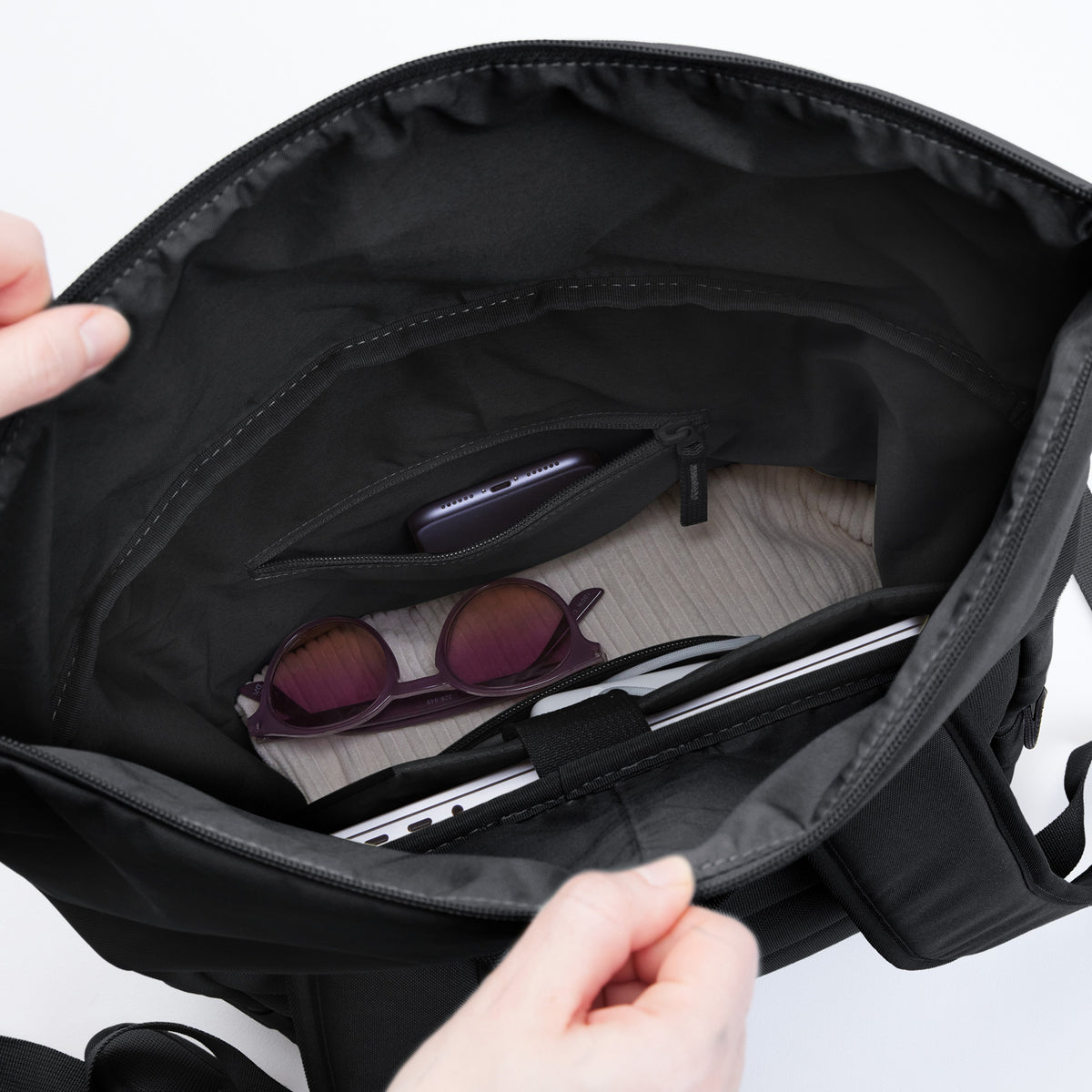 ROLLTOP EASY Rucksack in black (Schwarz), Hände halten ihn offen, innen Handy, Sonnenbrille und Laptop.