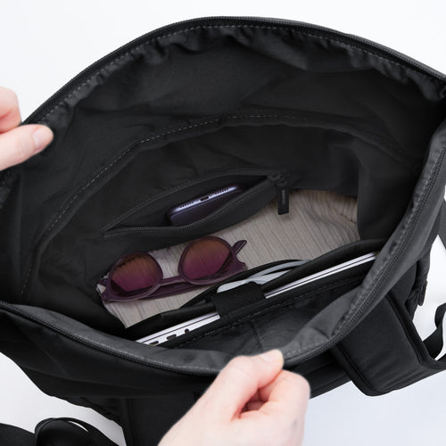 ROLLTOP EASY Rucksack in black (Schwarz), Hände halten ihn offen, innen Handy, Sonnenbrille und Laptop.