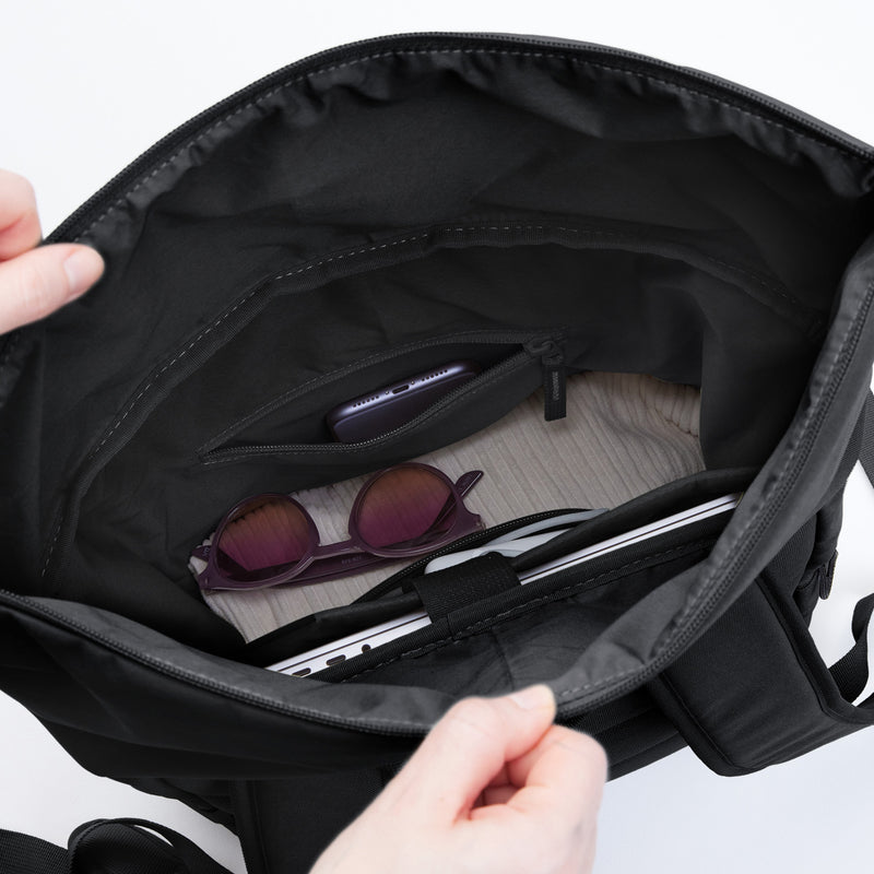 ROLLTOP EASY Rucksack in black (Schwarz), Hände halten ihn offen, innen Handy, Sonnenbrille und Laptop.