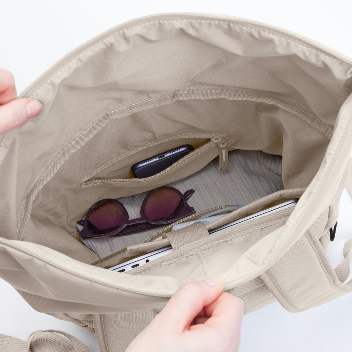 ROLLTOP EASY Rucksack in soft shell (warmes Cremeweiß) mit Blick in den Innenraum mit Laptop, Sonnenbrille und Smartphone.