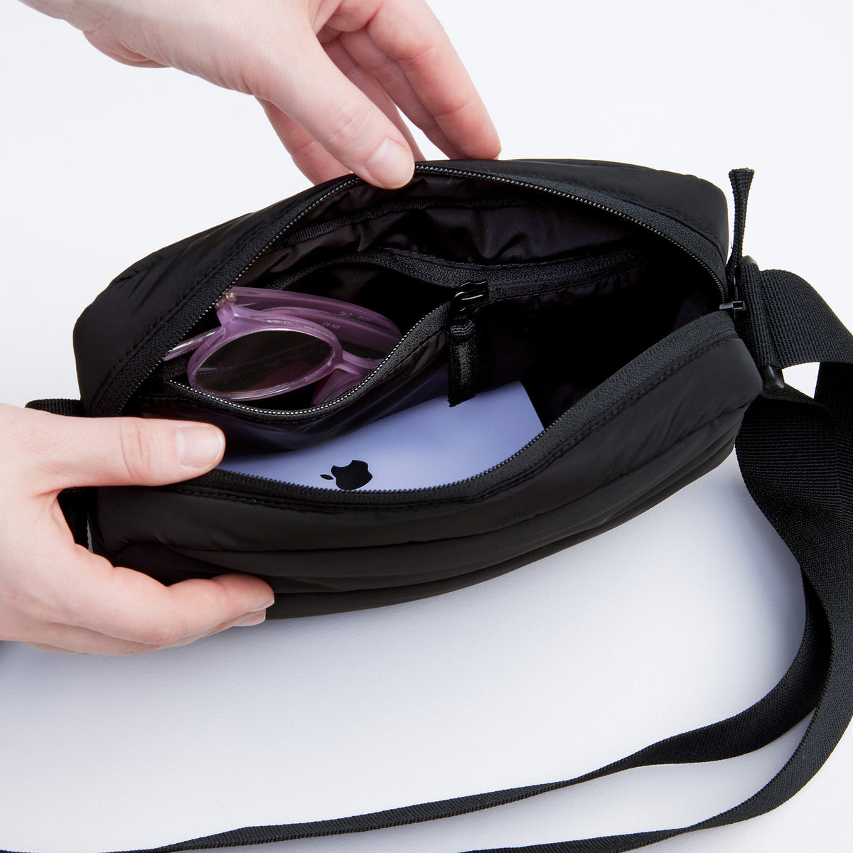PUFFER CROSSBODY BAG Tasche in black (Schwarz) von einer Frau geöffnet.