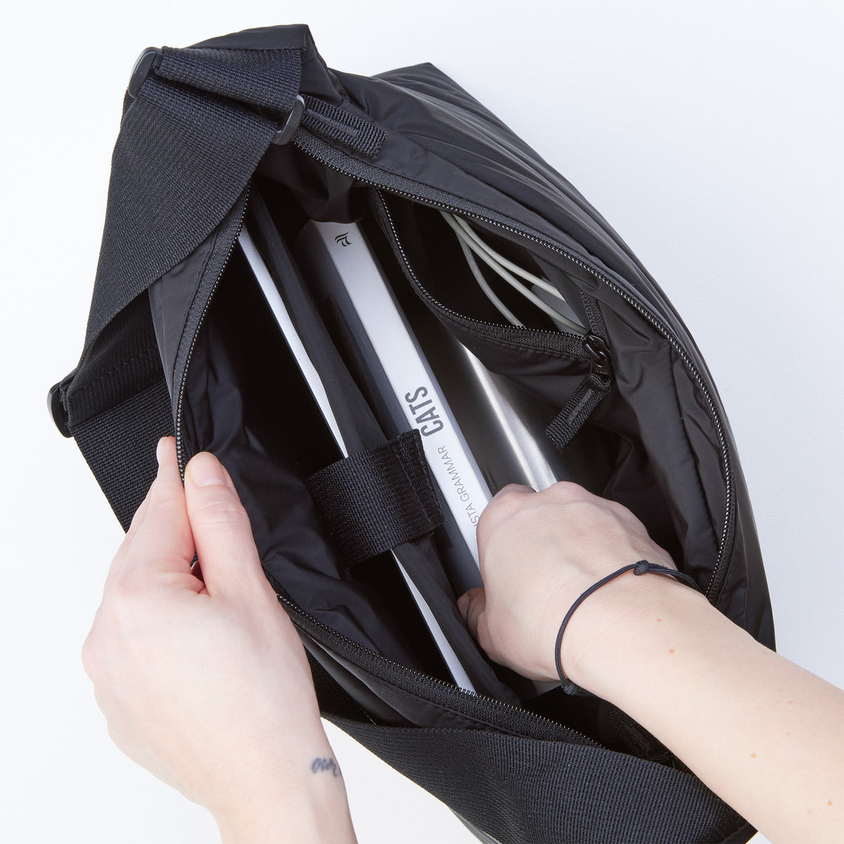 PUFFER SQUARE BAG Tasche in black (Schwarz), von einer Frau geöffnet und bestückt.