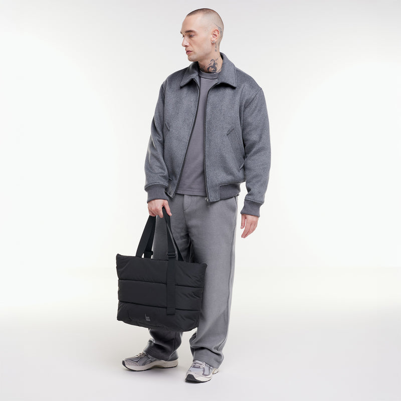 PUFFER TOTE BAG Tasche in black (Schwarz) von einem Mann in der Hand gehalten.