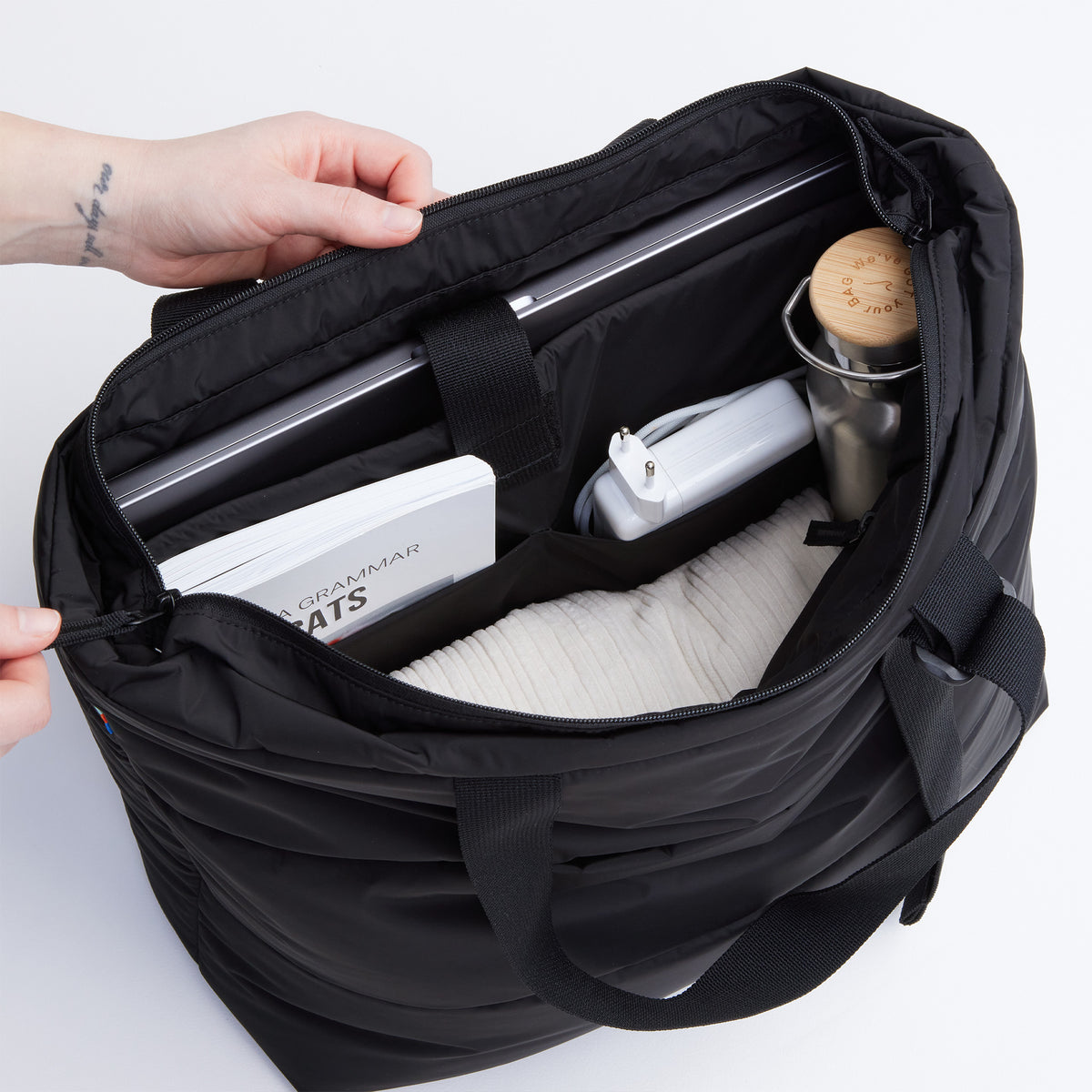 PUFFER TOTE BAG Tasche in black (Schwarz) von einer Person geöffnet, mit Laptop und Gegenständen im Inneren.