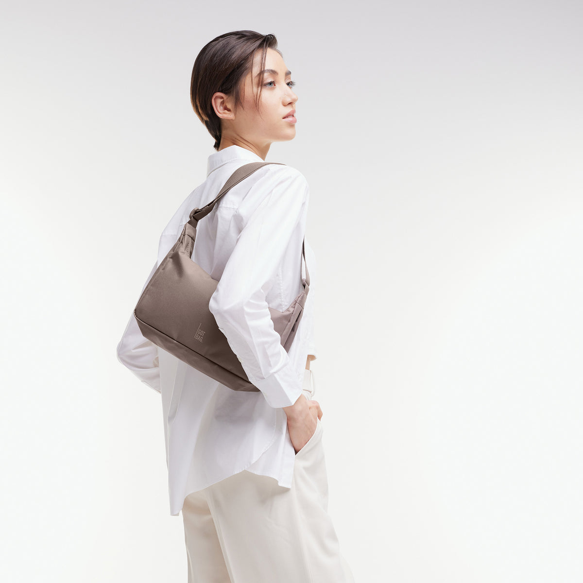 SQUARE BAG SMALL Tasche in oyster (klassisches Taupe-Braun) von einer Frau über der Schulter getragen.