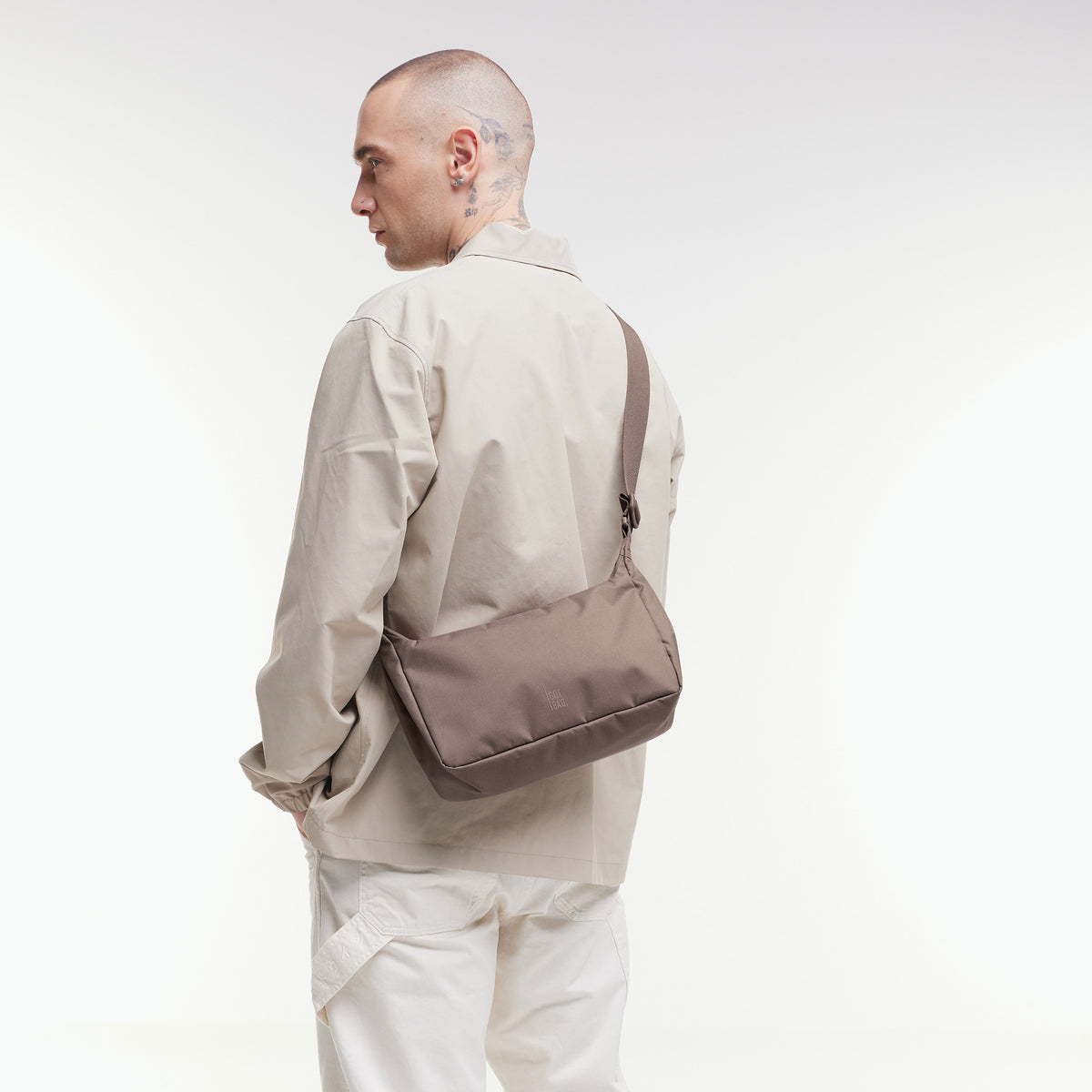 SQUARE BAG SMALL Tasche in oyster (klassisches Taupe-Braun) von einem Mann über der Schulter getragen.