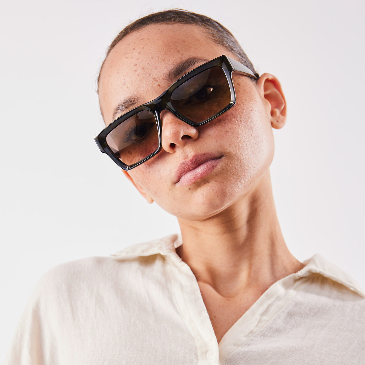 RE SHADES NO RE:SHADE von einer Frau mit Sommersprossen getragen, in Nahaufnahme auf hellem Hintergrund.