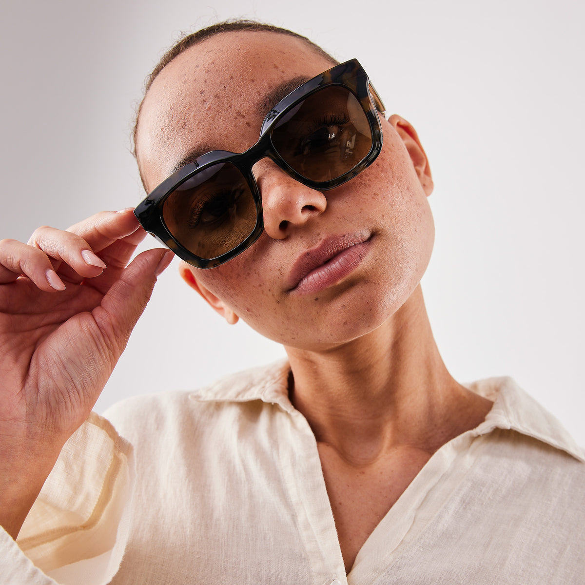 Eine Frau mit Sommersprossen trägt eine RE SHADES NO RE:SHADE in tortoise, die sie mit der Hand richtet.
