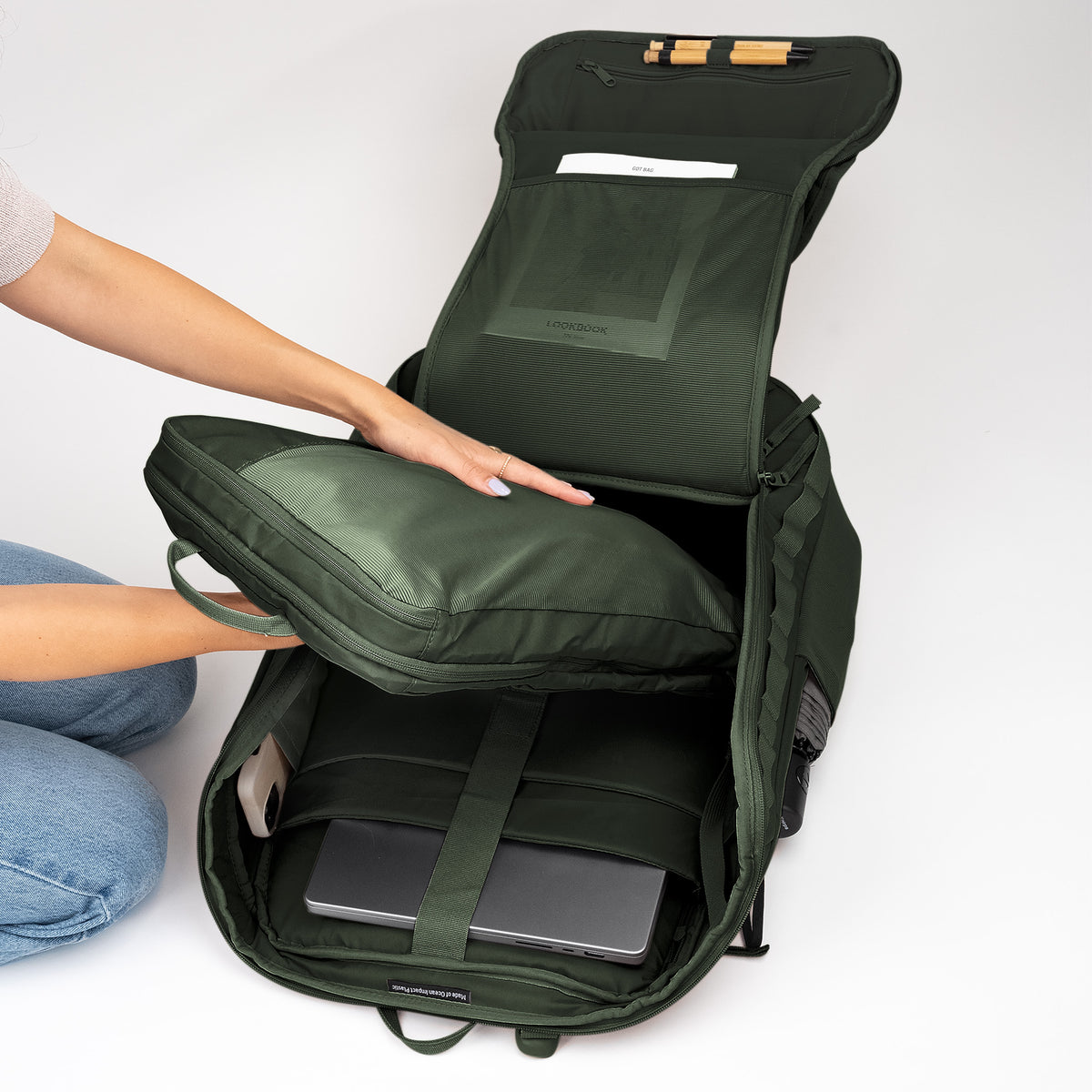 Eine Frau befüllt den PRO PACK TRAVEL Rucksack in algae (Dunkelgrün mit Graustich) mit einer Packtasche.