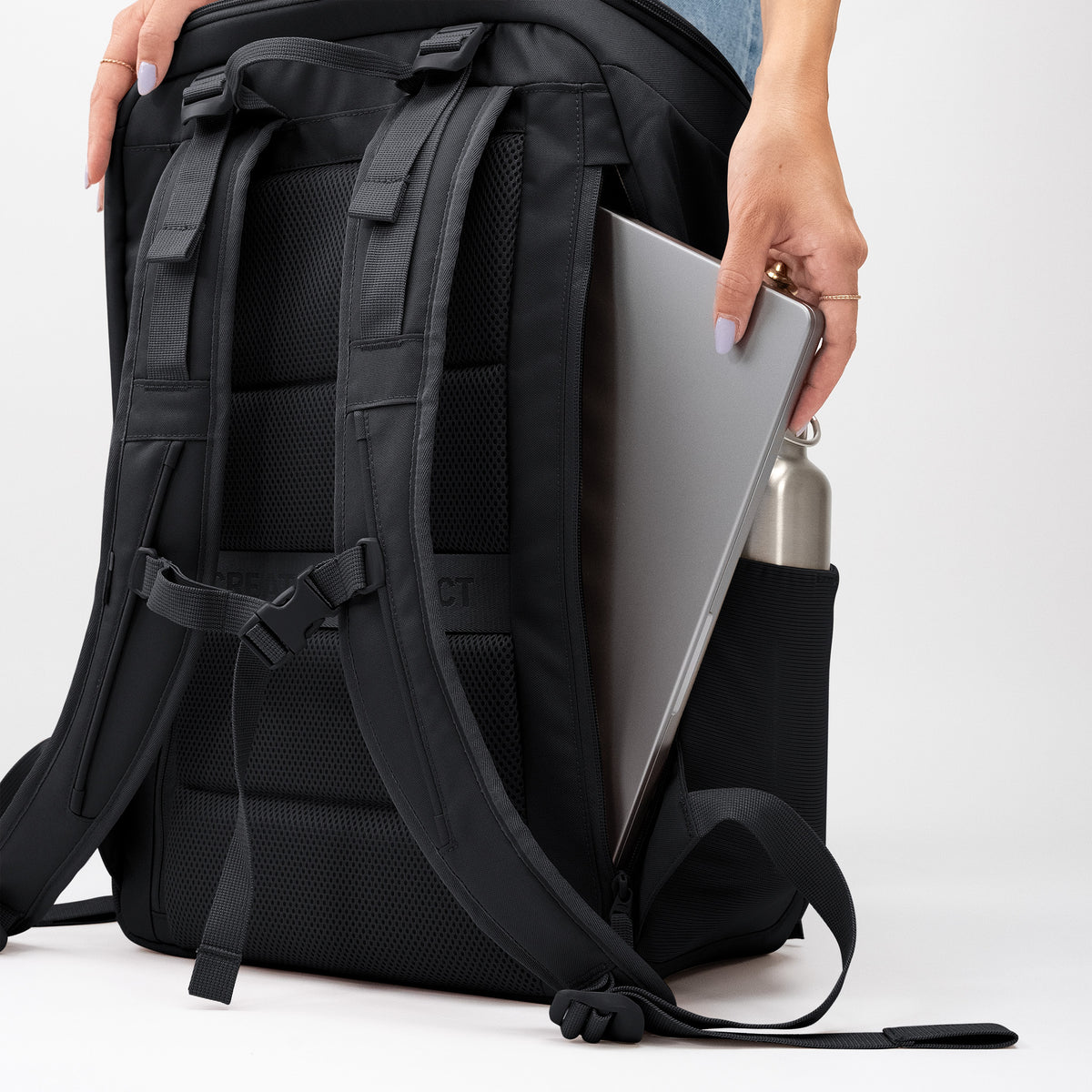 PRO PACK TRAVEL Rucksack in black (Schwarz), eine Frau legt Laptop und Wasserflasche hinein.