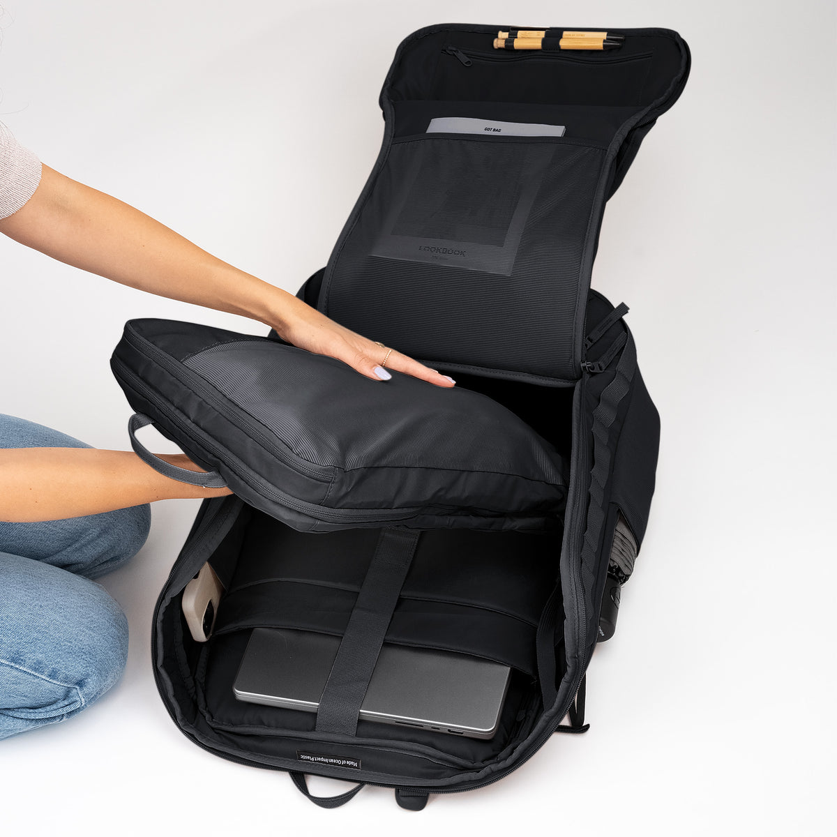 Eine Frau packt den geöffneten PRO PACK TRAVEL Rucksack in black (Schwarz), ein Etui wird hineingelegt.