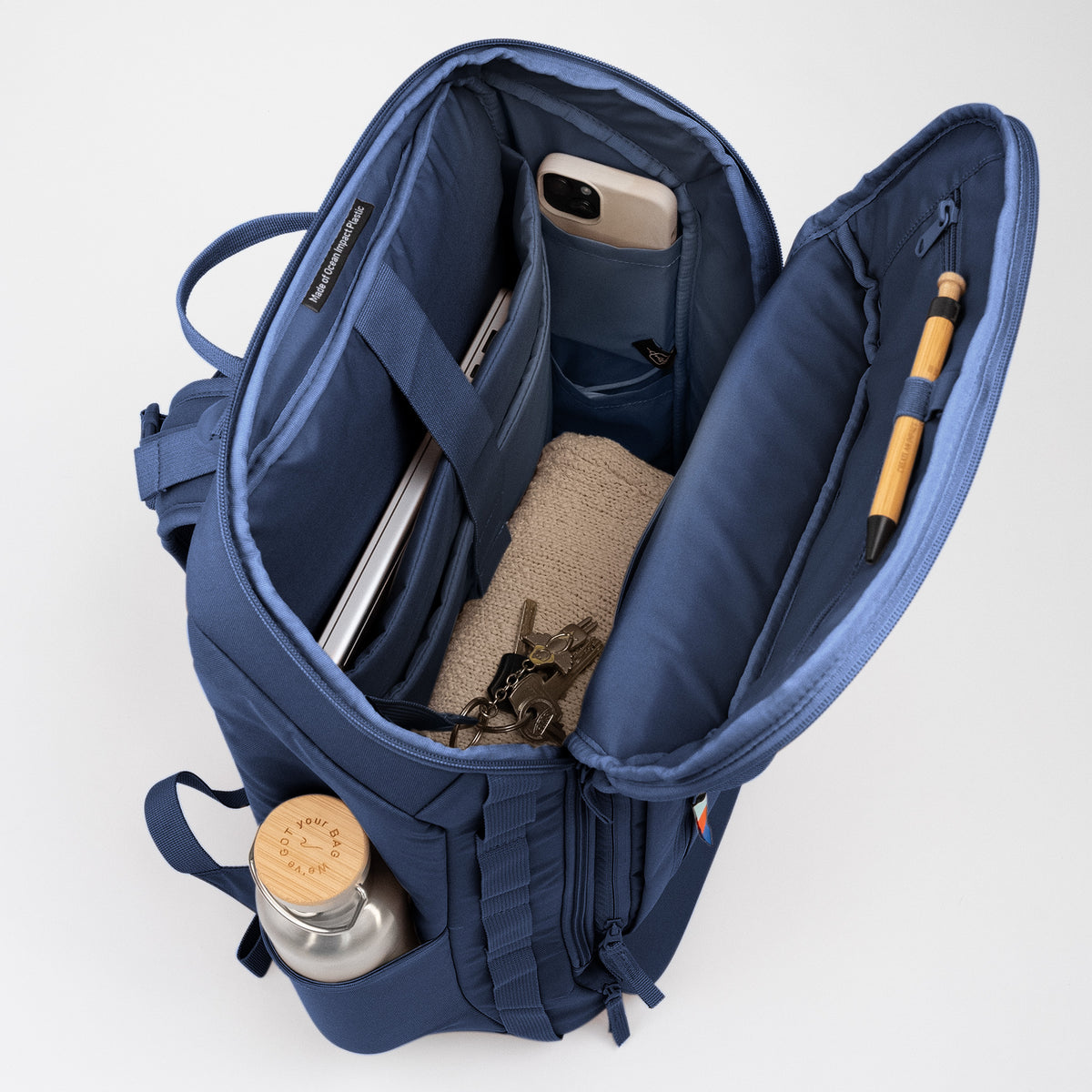 PRO PACK TRAVEL Rucksack oben geöffnet mit Laptop, Telefon, Schlüsseln, Stift, Trinkflasche. Innenetikett Made of Ocean Impact Plastic.