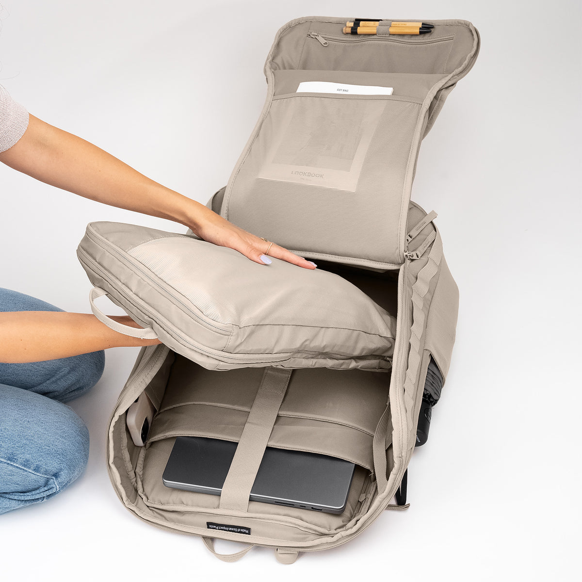 Eine Frau organisiert den PRO PACK TRAVEL Rucksack in scallop (helles Beige) und legt ein Fach hinein.