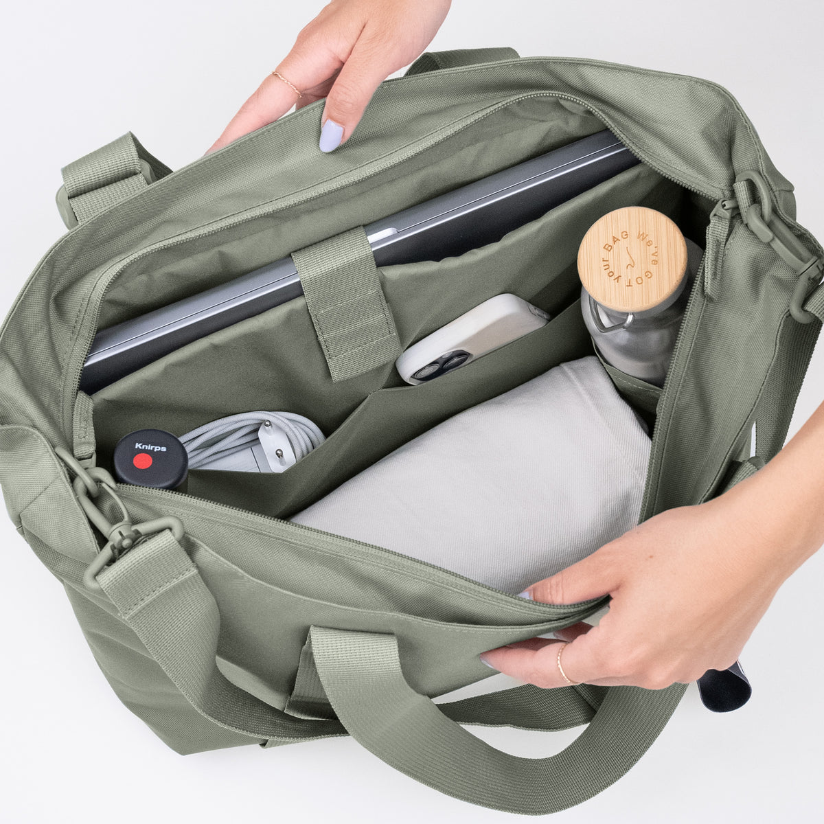 TOTE BAG Tasche in bass (Salbeigrün), von einer Frau geöffnet mit Blick auf den Inhalt.