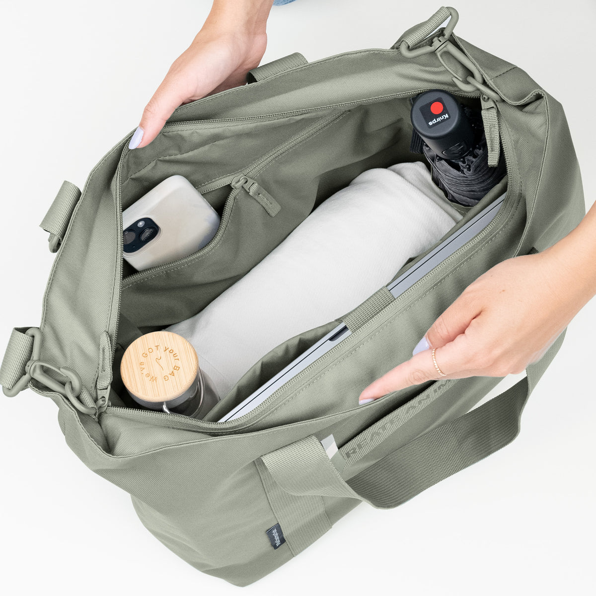 TOTE BAG MONOCHROME EDITION Tasche in bass (Salbeigrün), eine Frau organisiert den Inhalt im offenen Hauptfach.
