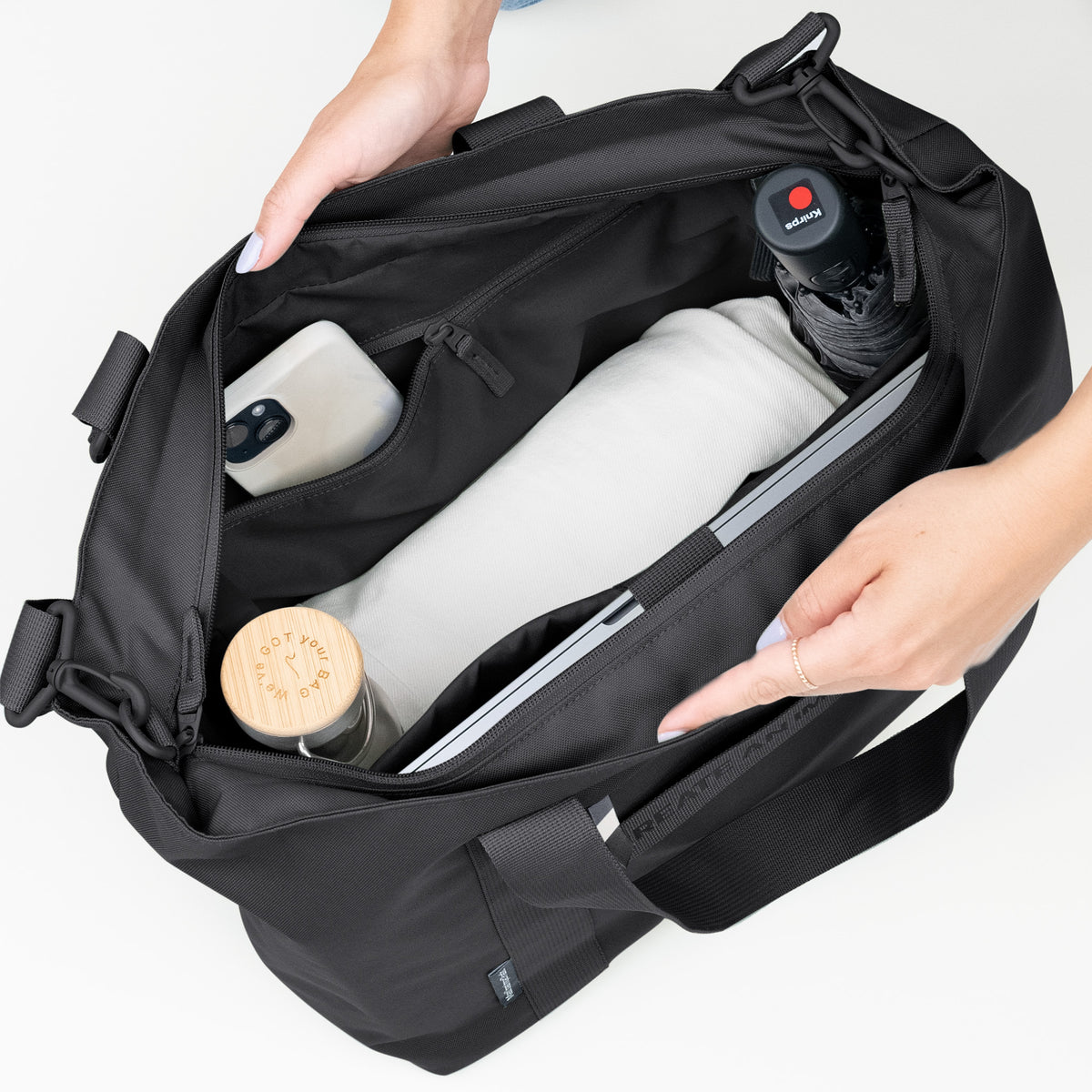 TOTE BAG Monochrome Edition Tasche in black (Schwarz) von einer Frau mit beiden Händen geöffnet, um den organisierten Innenraum zu zeigen.