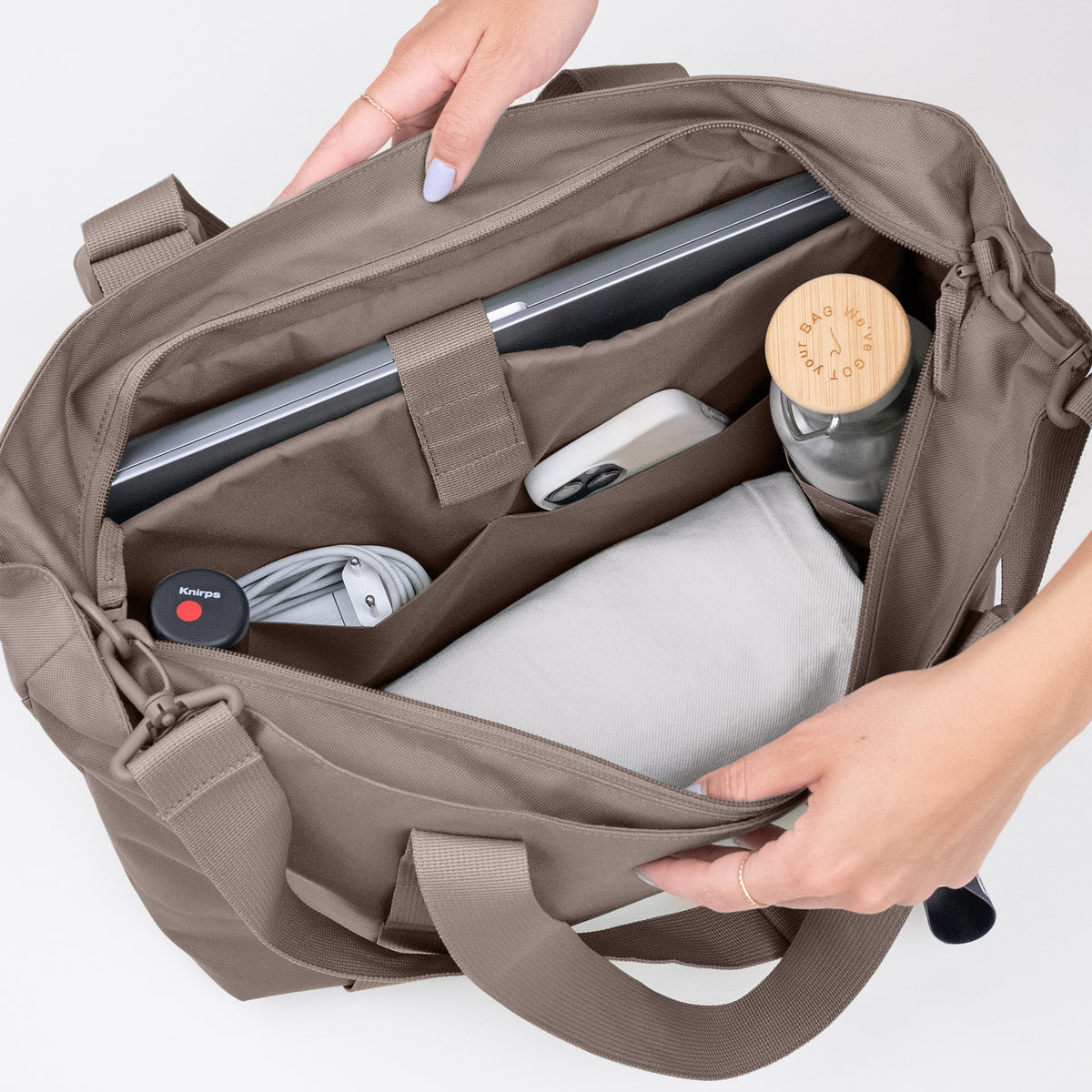Eine Frau hält die TOTE BAG Tasche in oyster (klassisches Taupe-Braun) offen und zeigt den Inhalt.