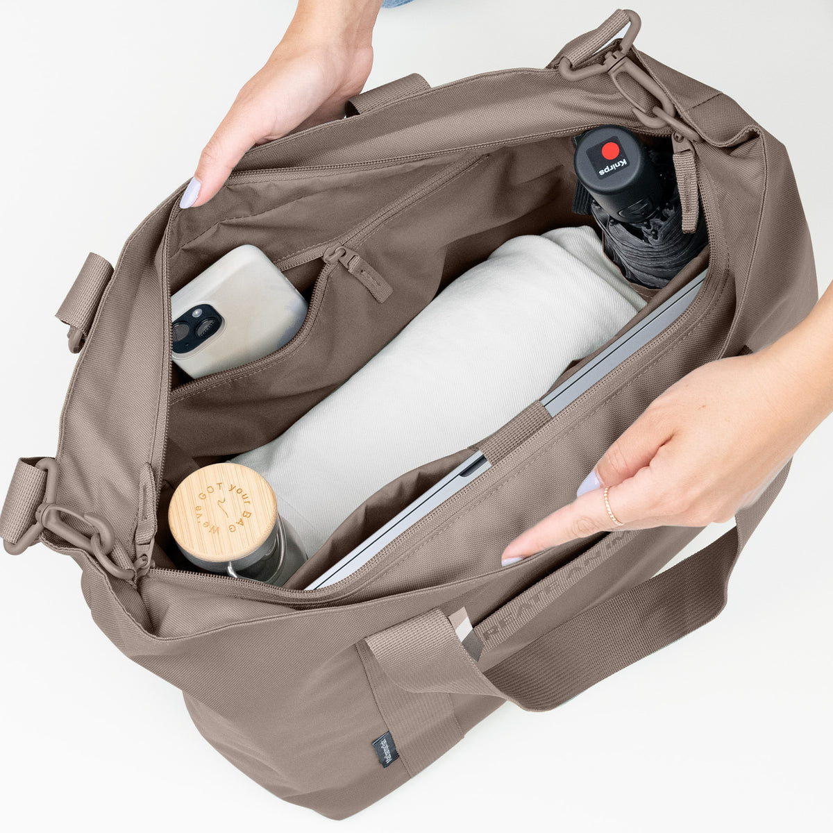 TOTE BAG Tasche in oyster (klassisches Taupe-Braun) von einer Frau geöffnet, mit Blick auf das organisierte Innere.