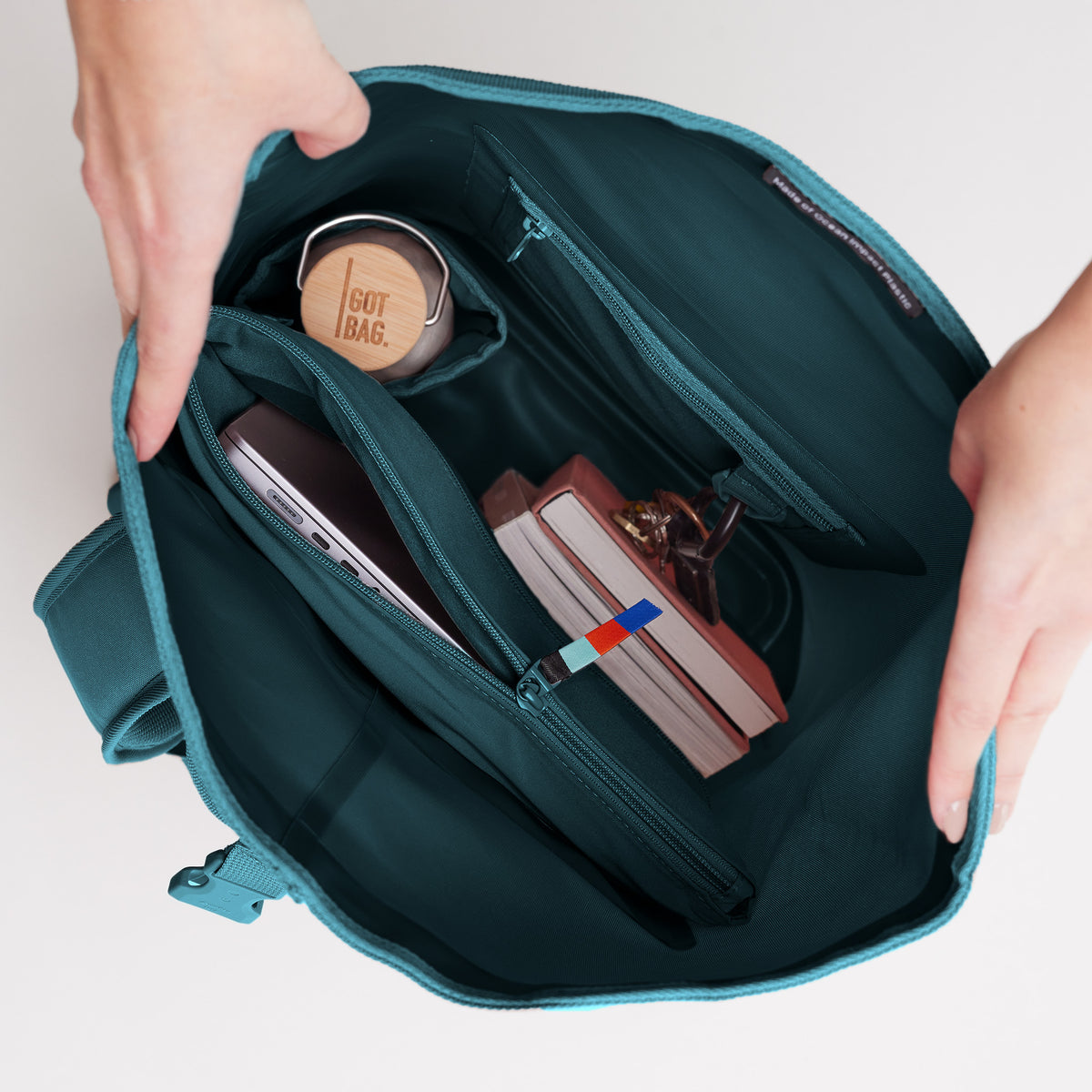 ROLLTOP LITE Rucksack in cliff (dunkles Petrol) mit geöffnetem Innenraum, der Laptop, Flasche und Bücher zeigt.