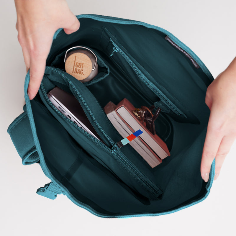 ROLLTOP LITE Rucksack in cliff (dunkles Petrol) mit geöffnetem Innenraum, der Laptop, Flasche und Bücher zeigt.
