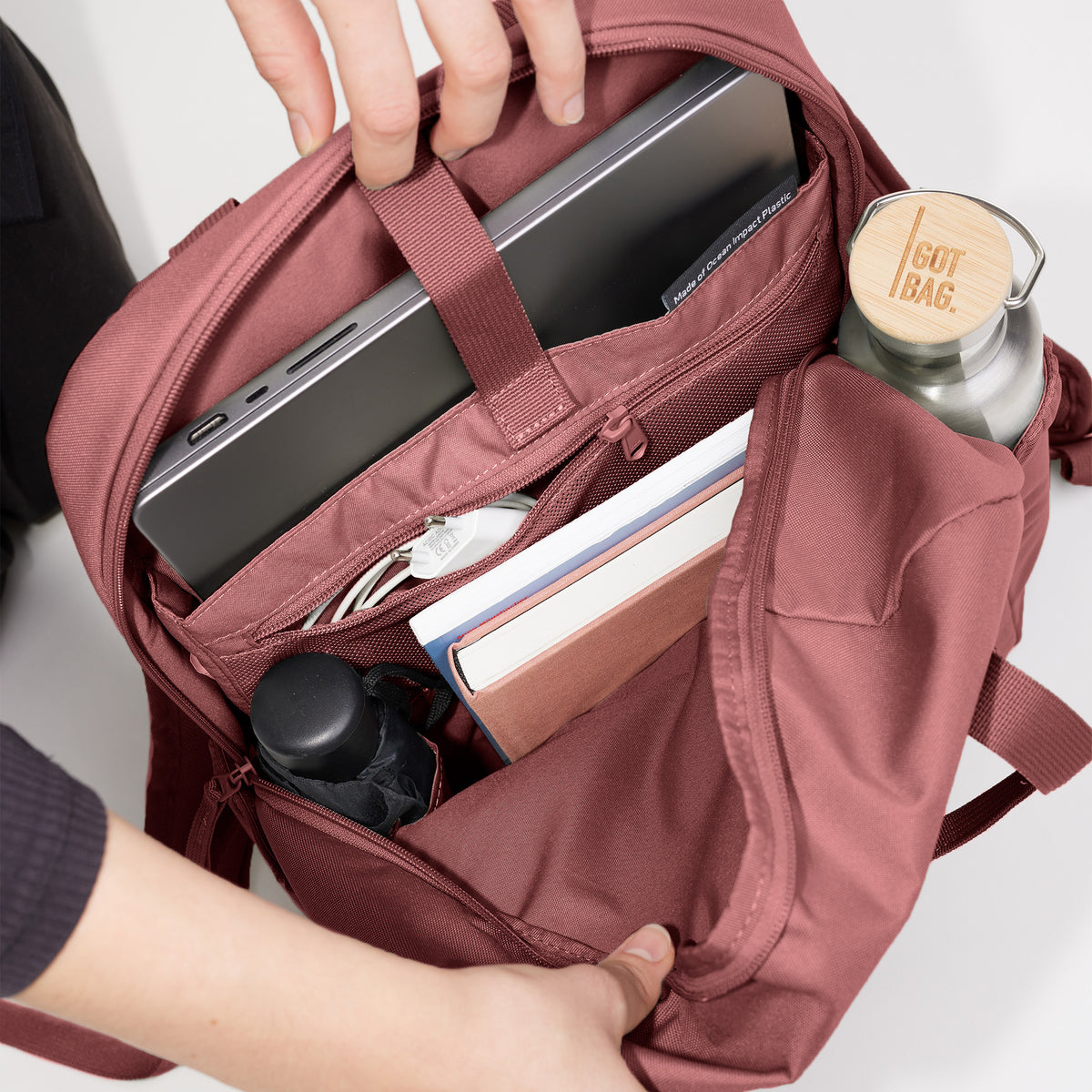 DAYPACK LOOP Rucksack in lionfish (dunkles Rosa mit Rotstich), von einer Frau geöffnet, zeigt Laptop und Bücher.