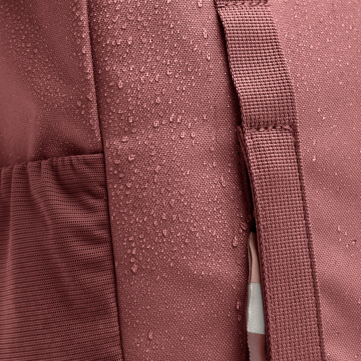 DAYPACK LOOP Rucksack in lionfish (dunkles Rosa mit Rotstich) als Detailaufnahme mit Wassertropfen auf dem Stoff.