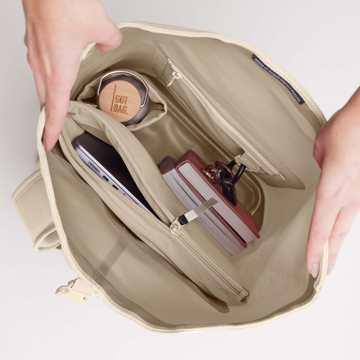 ROLLTOP Rucksack in salt (warmes Cremeweiß), von Händen geöffnet, zeigt Innenraum mit Laptop, Flasche, Büchern.