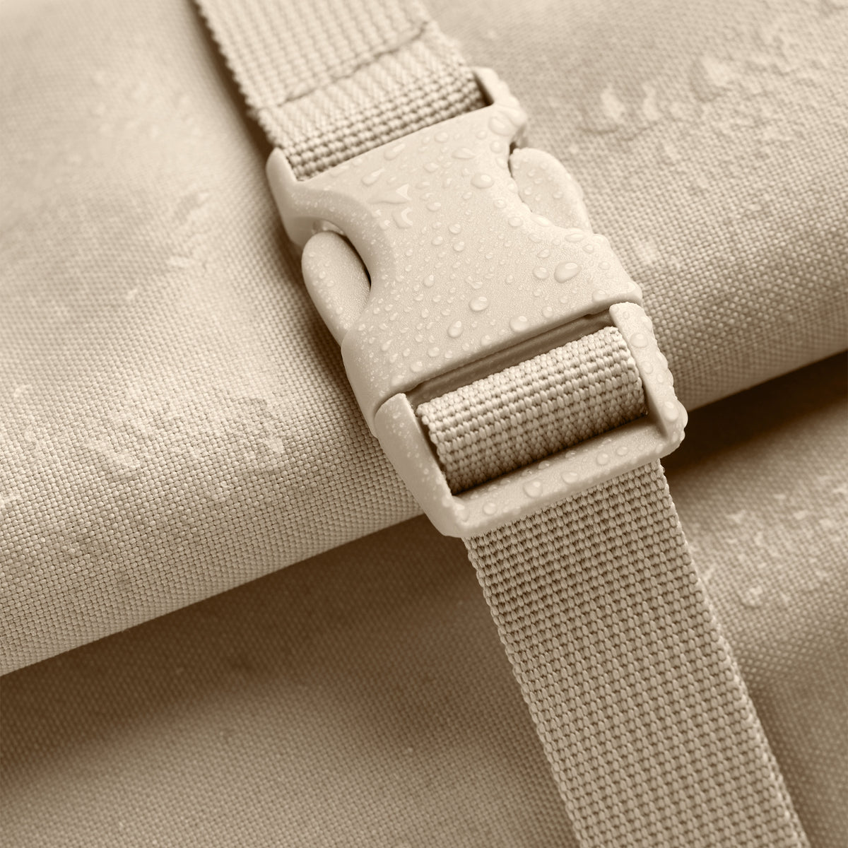 ROLLTOP LITE MONOCHROME EDITION Rucksack in salt (warmes Cremeweiß) mit Wassertropfen auf Stoff und Schnalle als Detailaufnahme.