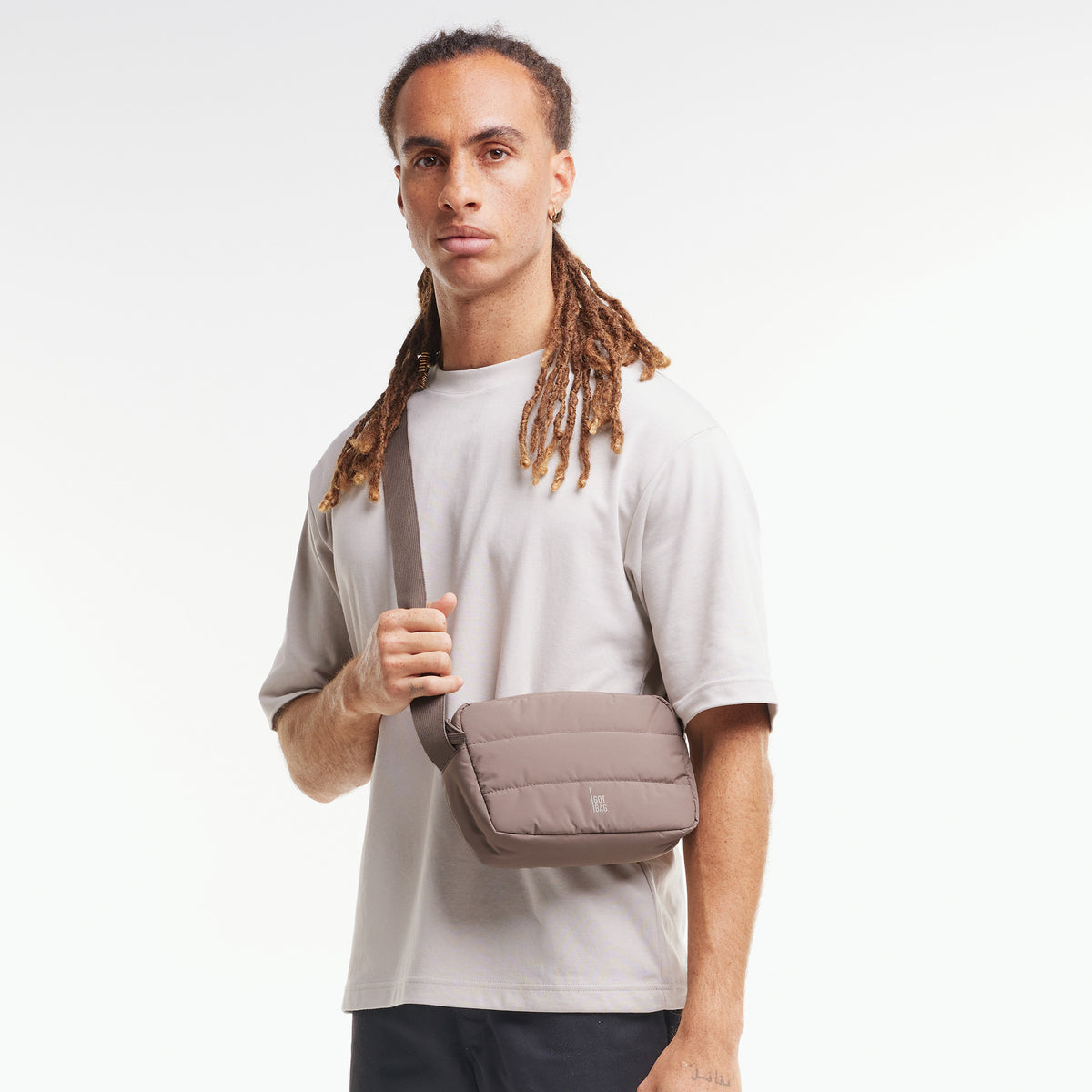 PUFFER CROSSBODY BAG Tasche in oyster (klassisches Taupe-Braun) von einem Mann crossbody getragen.