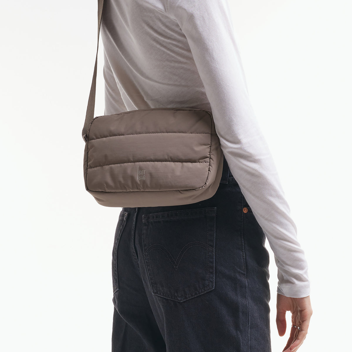 PUFFER CROSSBODY BAG Tasche in oyster (klassisches Taupe-Braun) von einer Frau crossbody getragen.